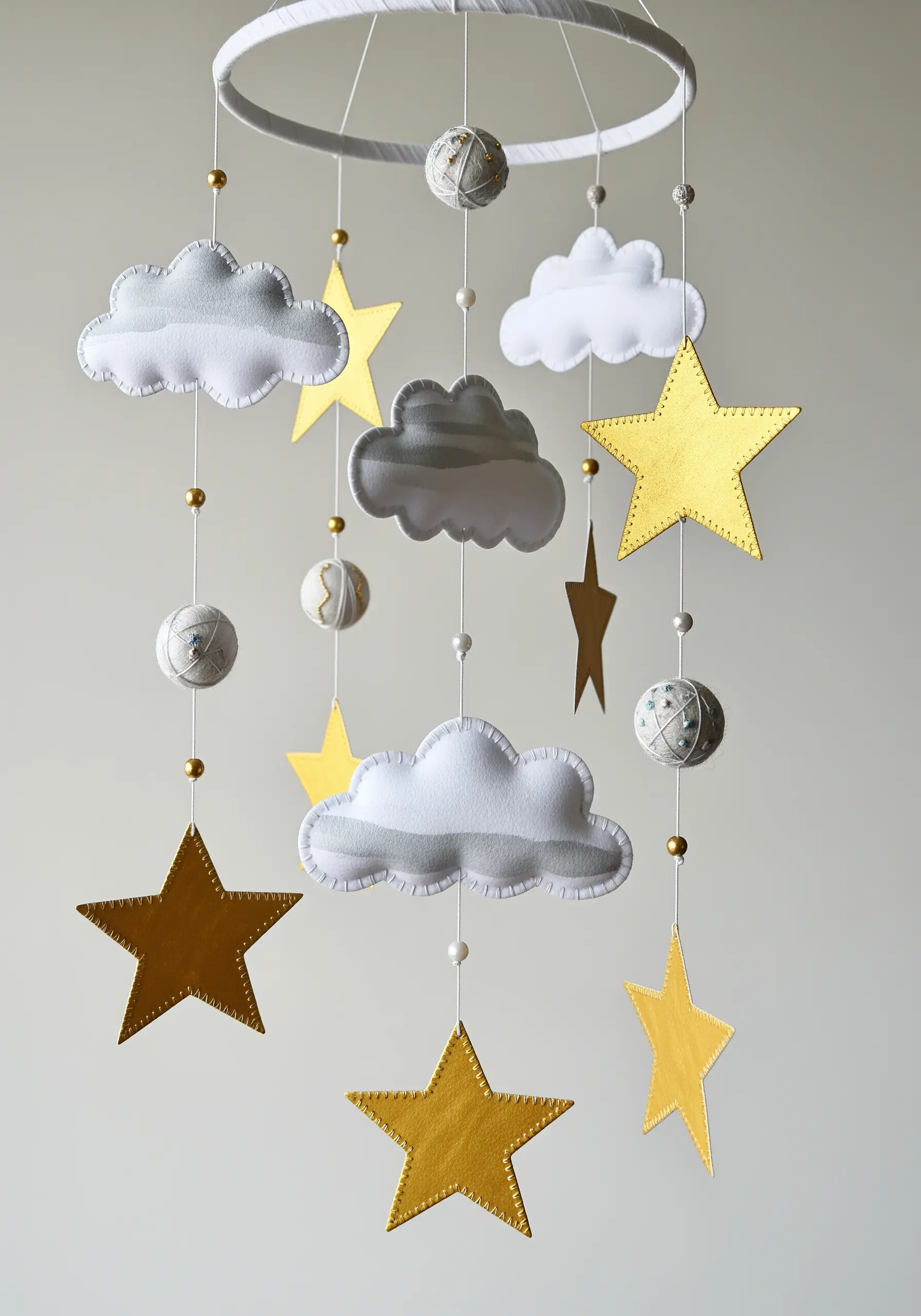 A nursery mobile featuring stitched gray and white felt clouds and painted gold paper stars.