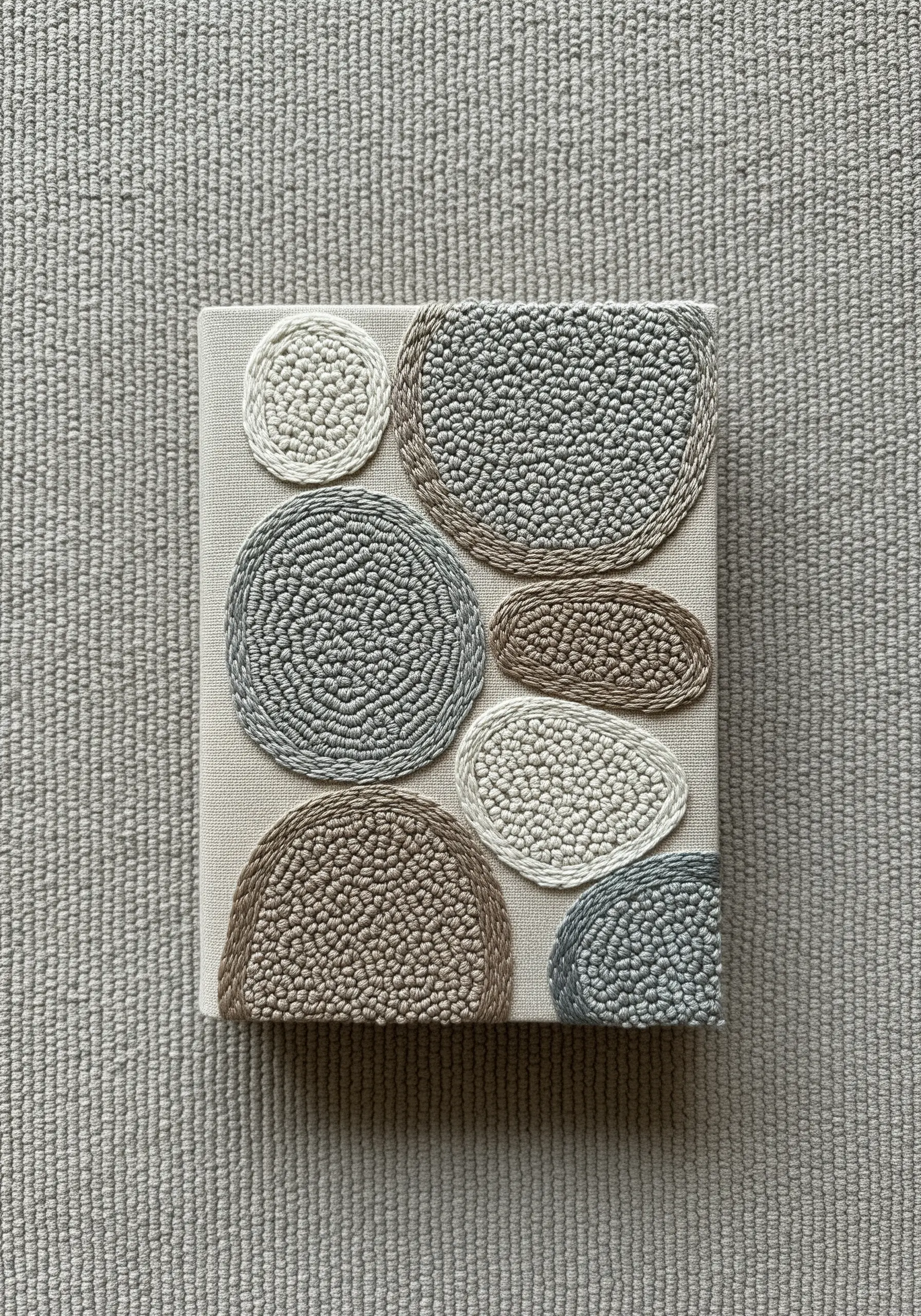 Abstract art with pebble shapes filled with punch needle loops in neutral tones.