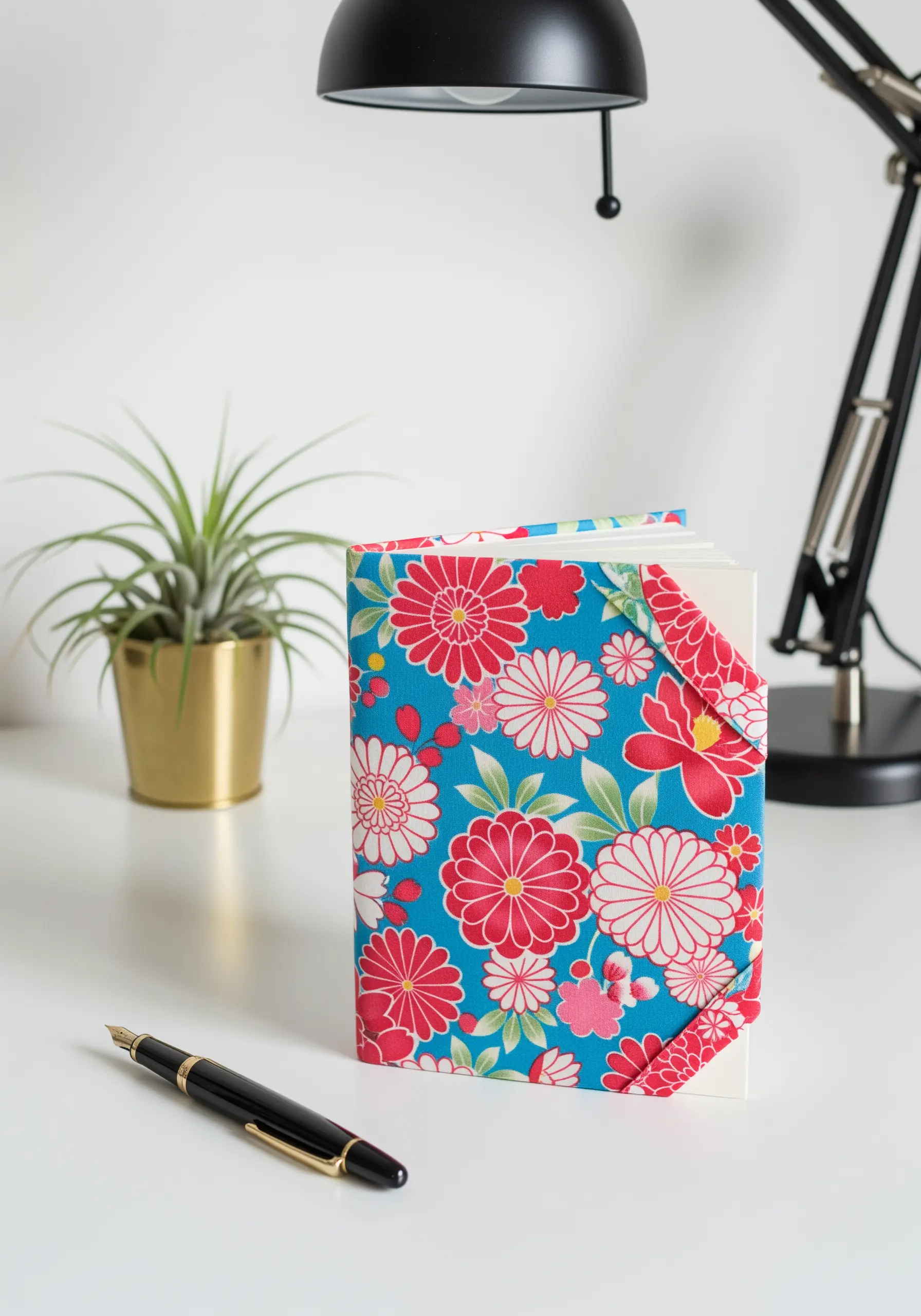 A journal with a colorful, Japanese-inspired floral fabric cover on a white desk.