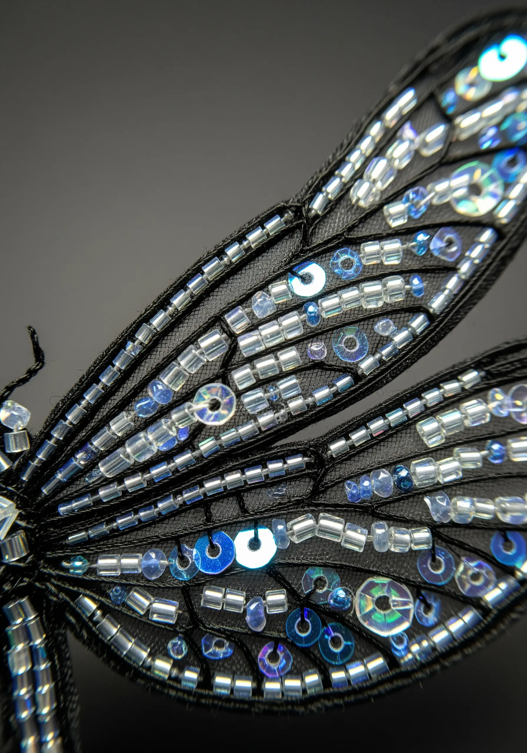 A close-up of a dragonfly wing created with iridescent seed beads and sequins on black tulle.