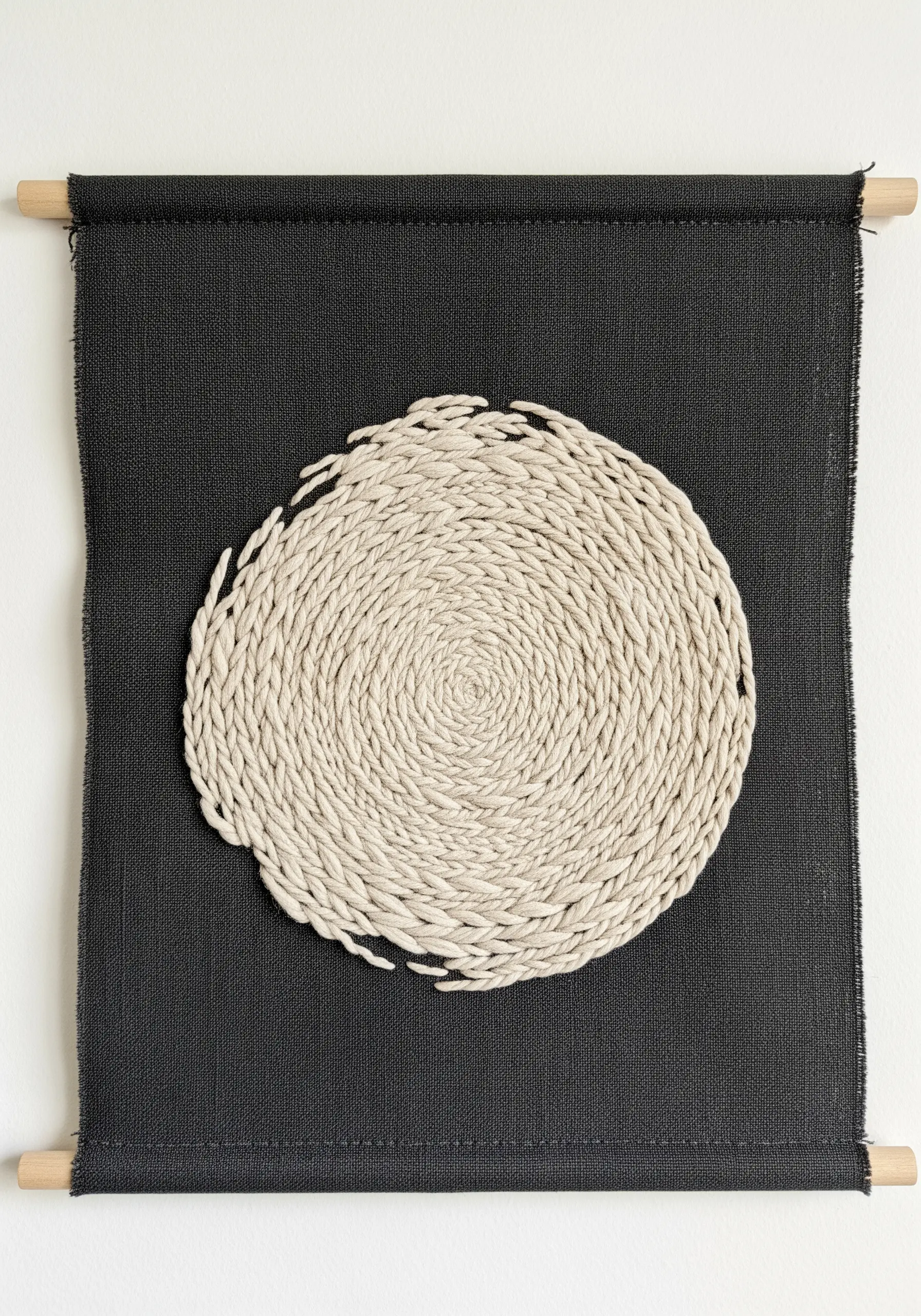 A single coiled rope circle stitched onto a dark fabric wall hanging.
