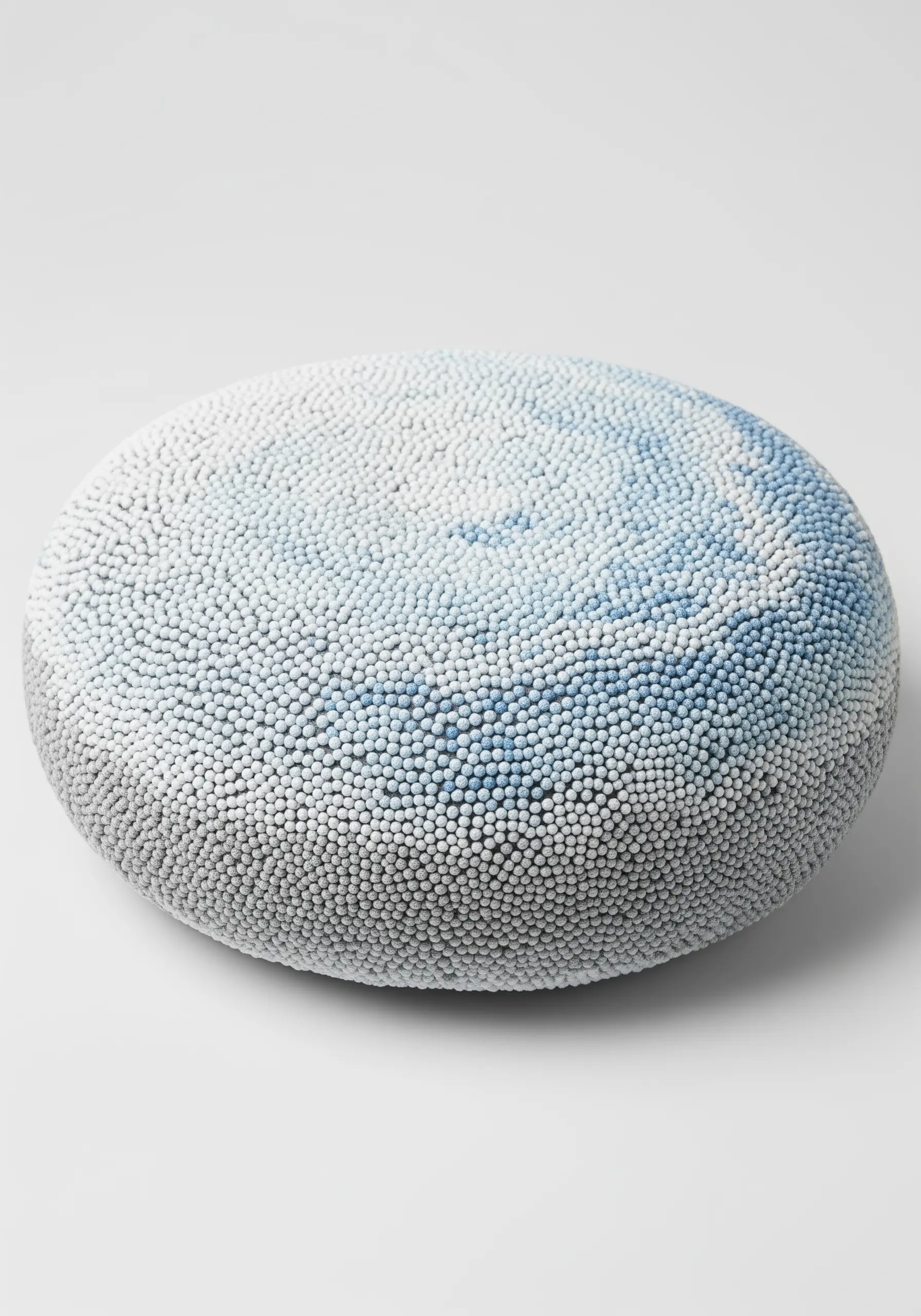 A round cushion covered in a dense gradient of white, blue, and grey French knots.