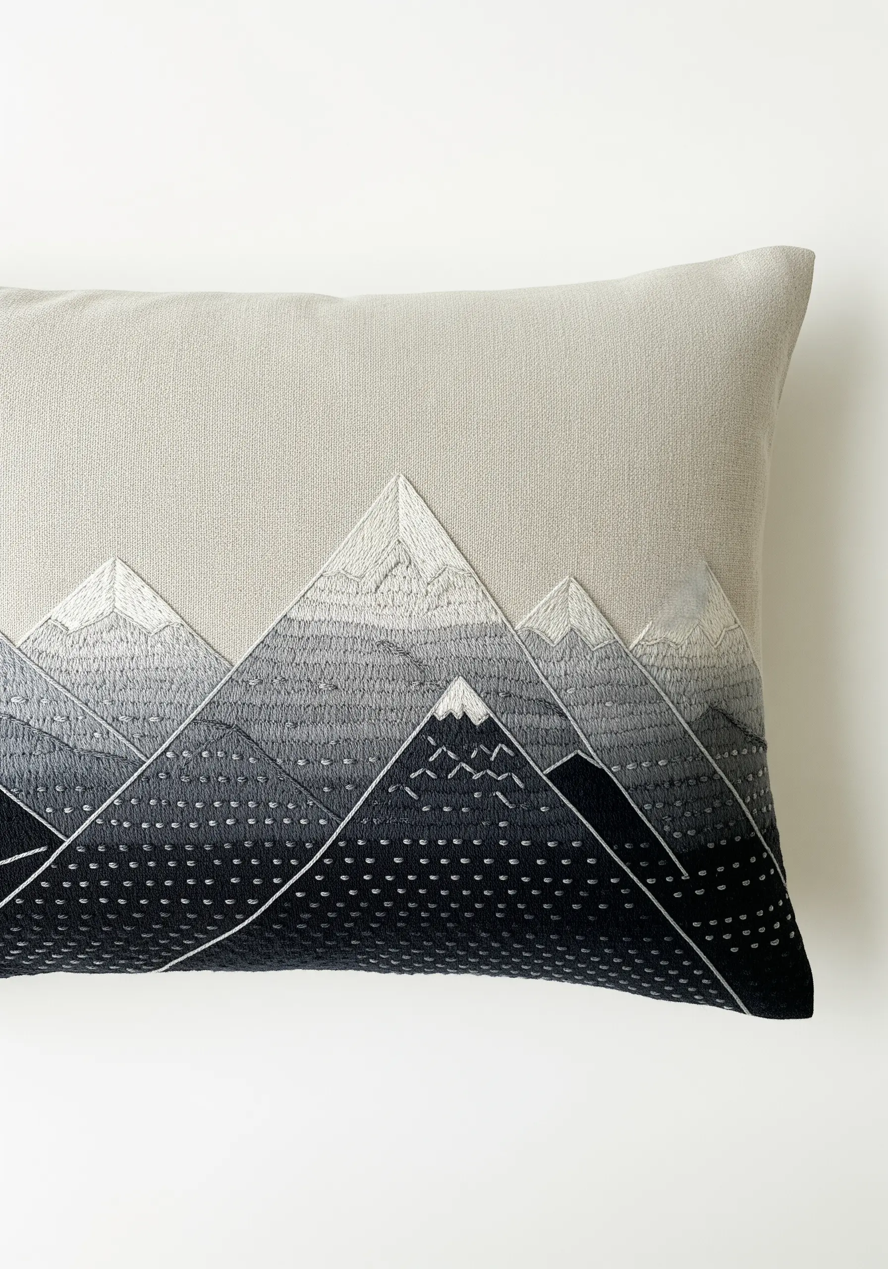 Monochrome mountain range embroidered on a grey cushion with gradient shading and textural stitches.