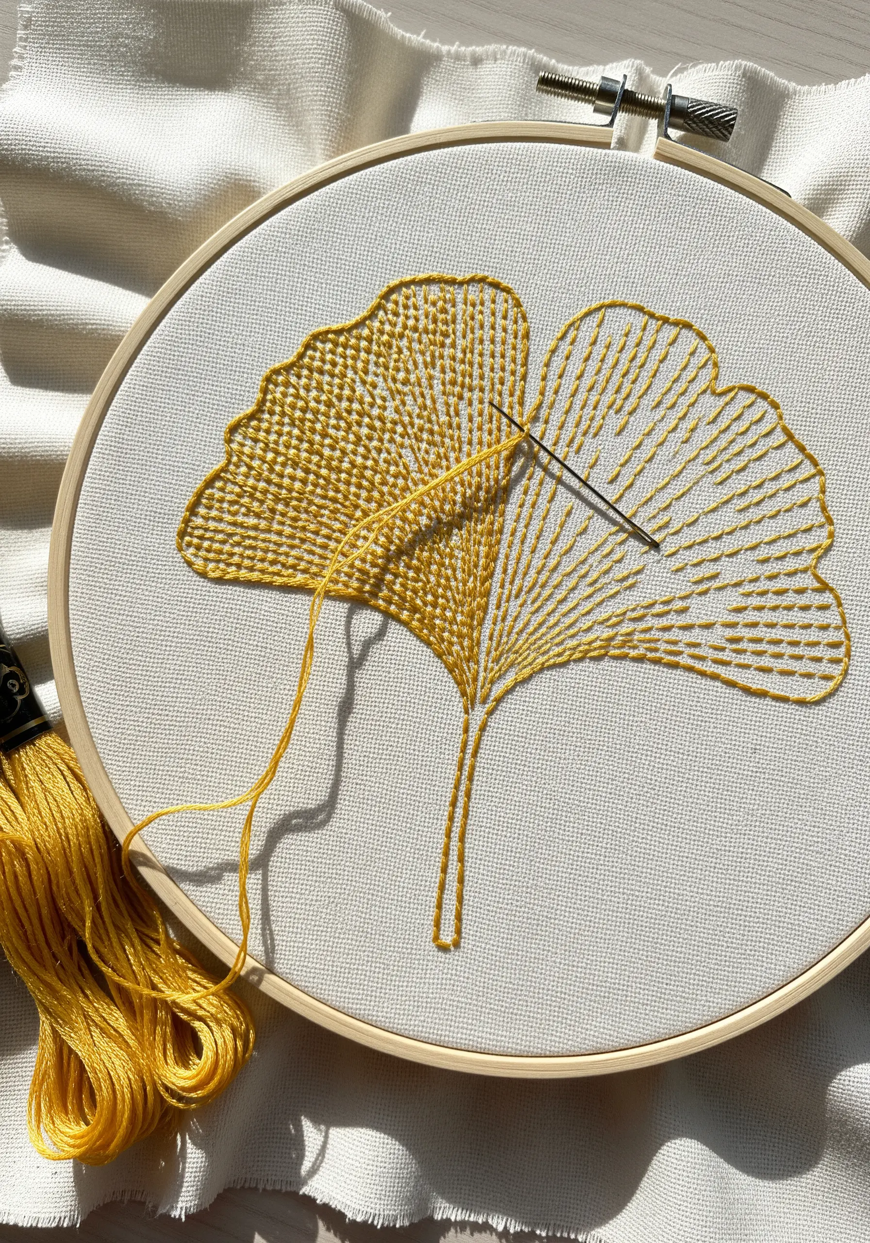 A ginkgo leaf being embroidered in yellow, with one side filled and the other outlined.