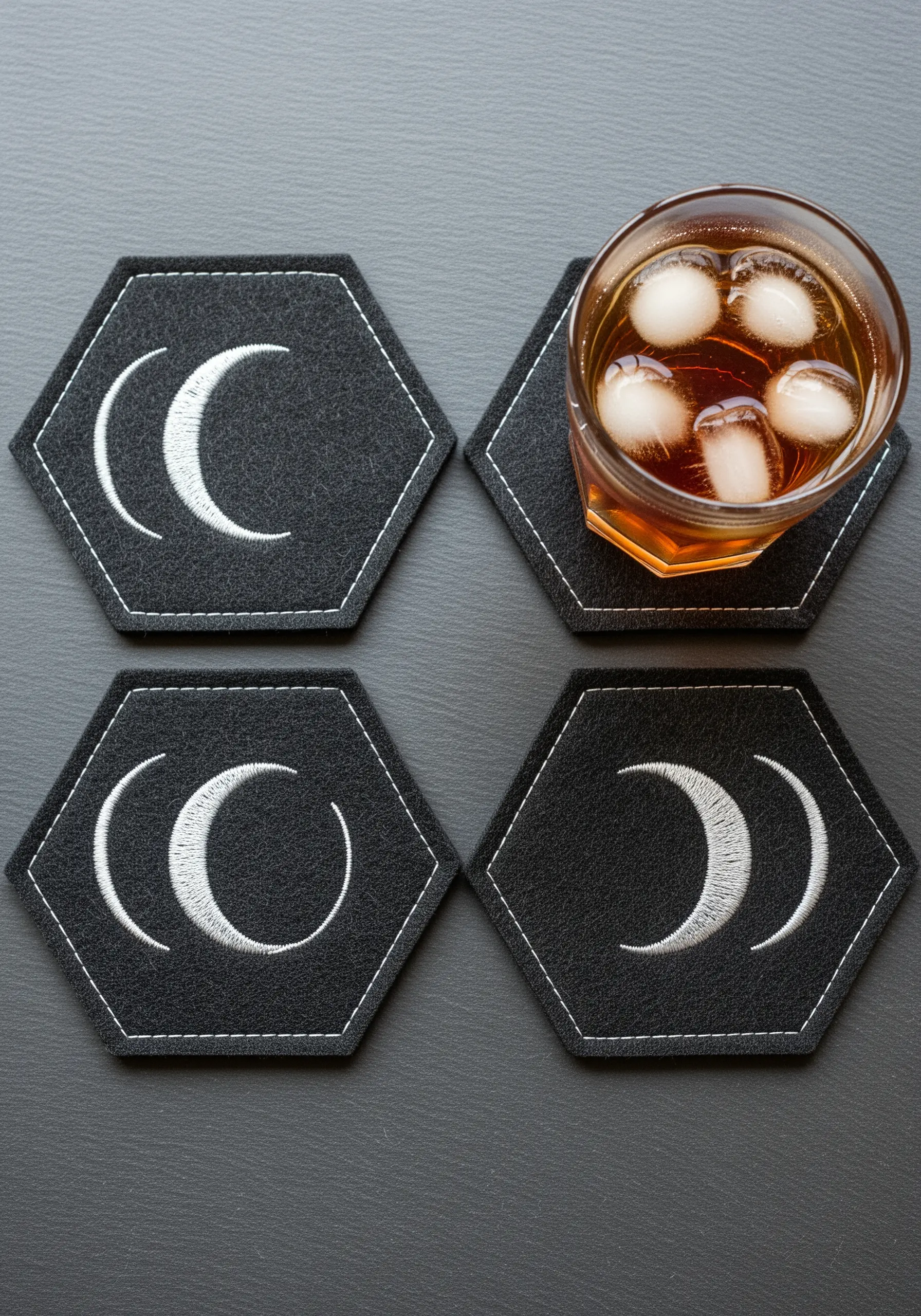 Minimalist moon phase designs in white thread on black hexagonal felt coasters
