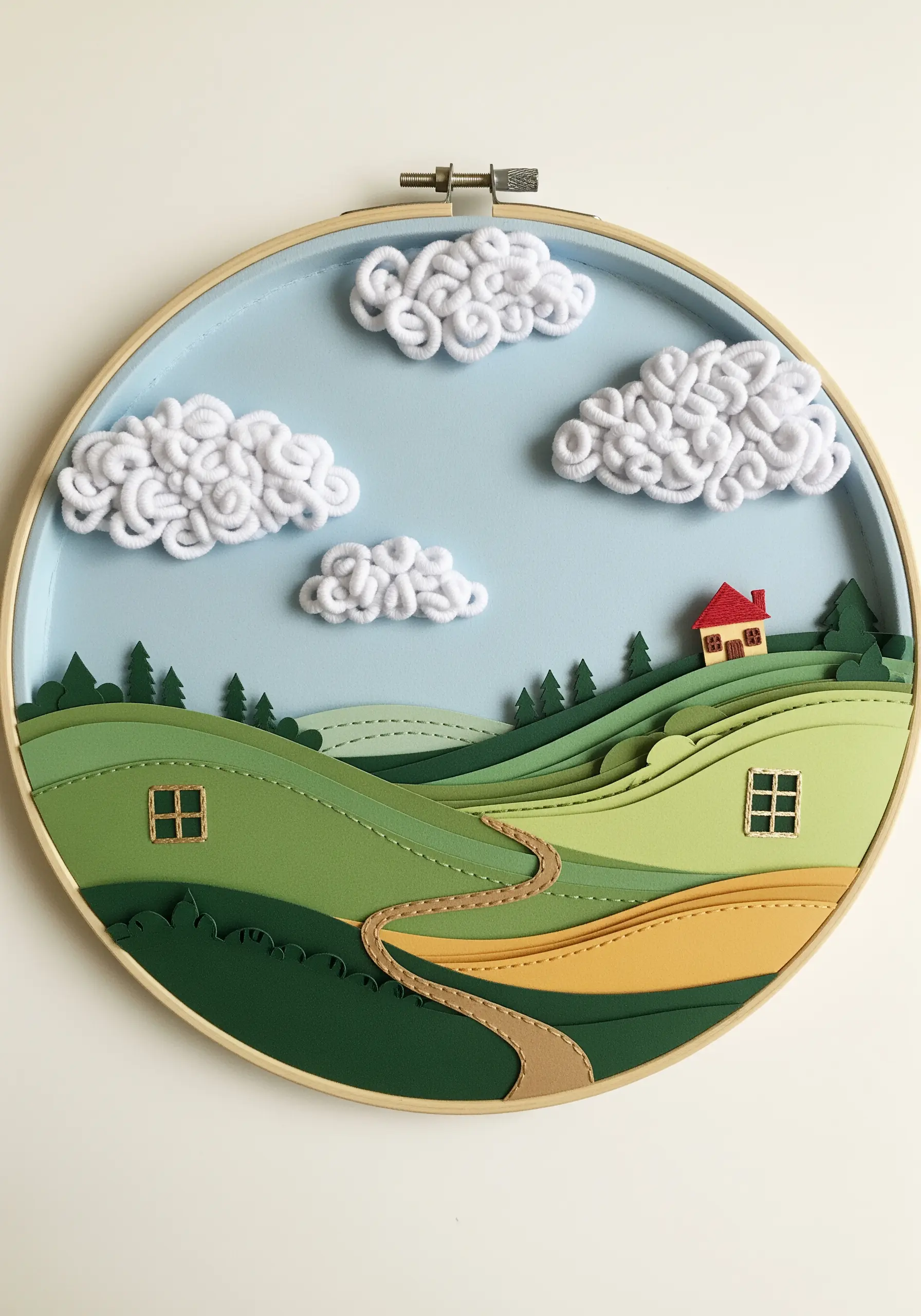 A layered paper landscape in a hoop with textured yarn clouds.