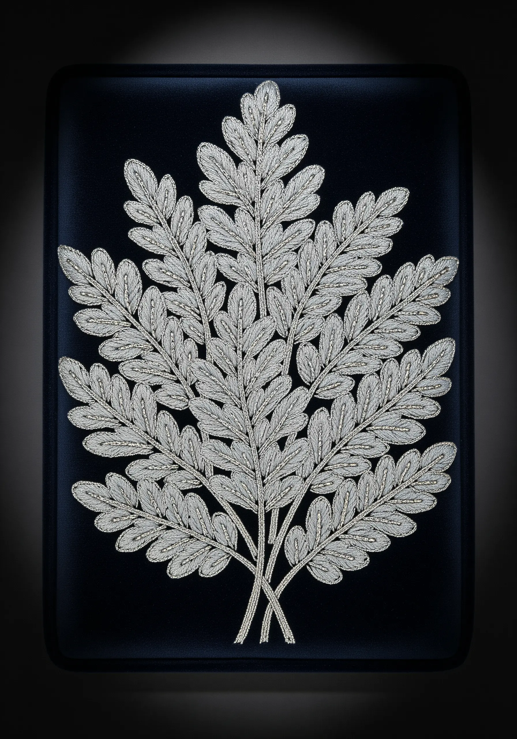 An intricate fern stitched entirely in silver thread on a black velvet background.