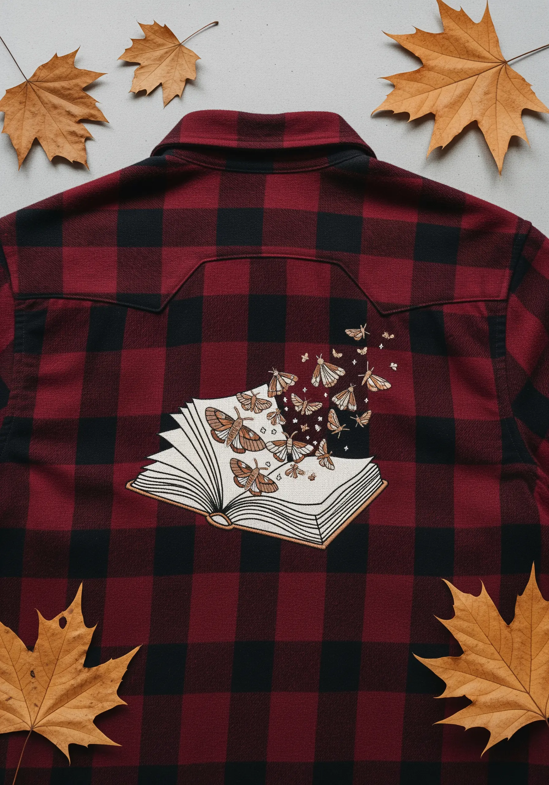 An open book embroidered on the back of a red and black flannel shirt, with moths flying out.