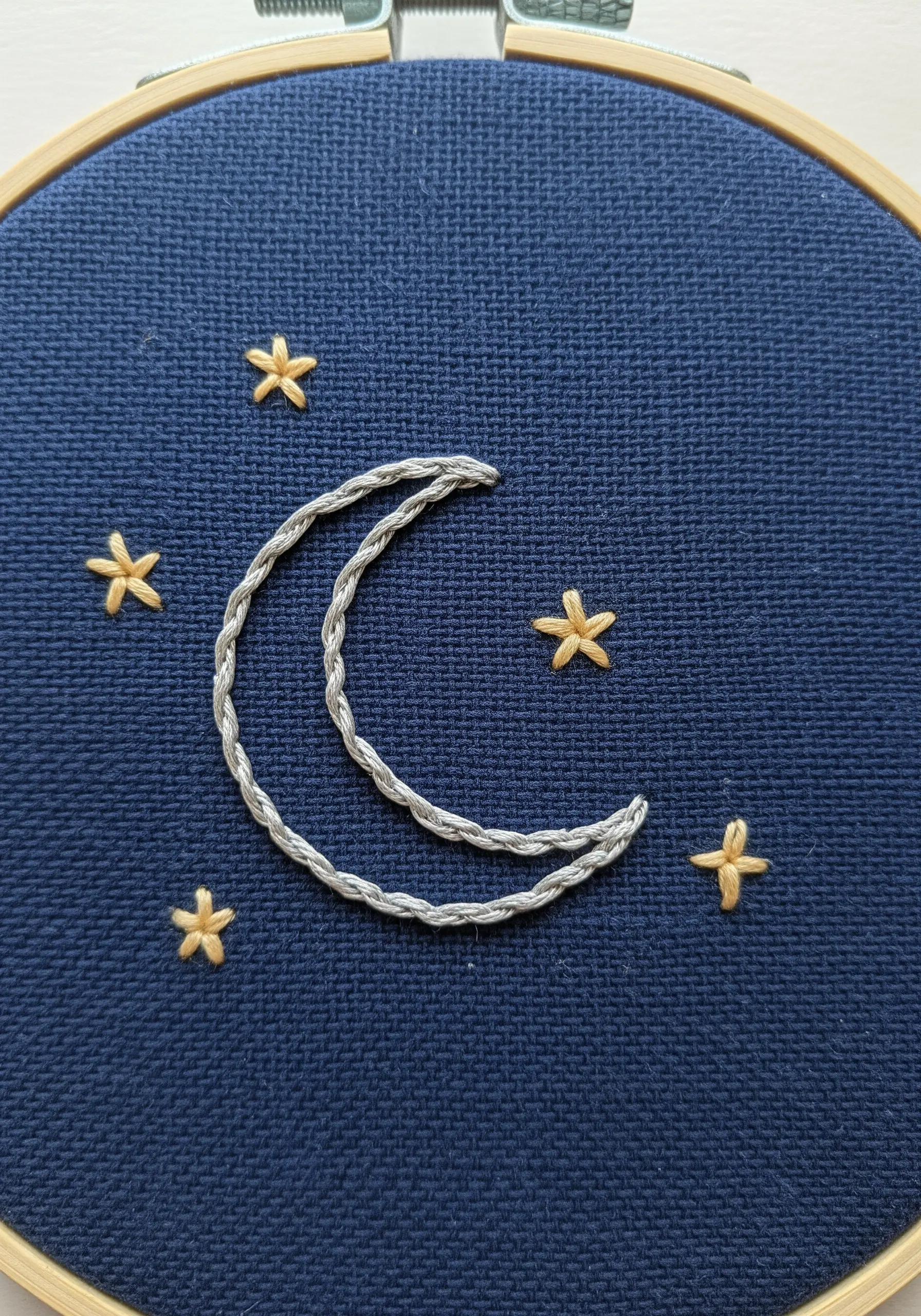 A crescent moon and stars embroidered on dark blue Aida cloth.