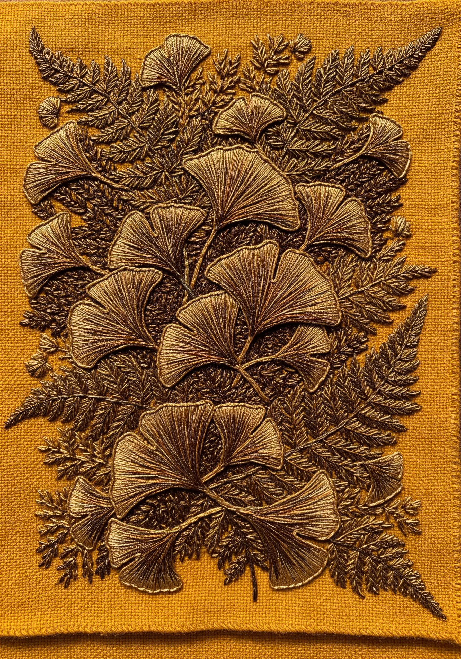 Dense, textured bronze-tone embroidery of ginkgo and ferns on a mustard-yellow textile.