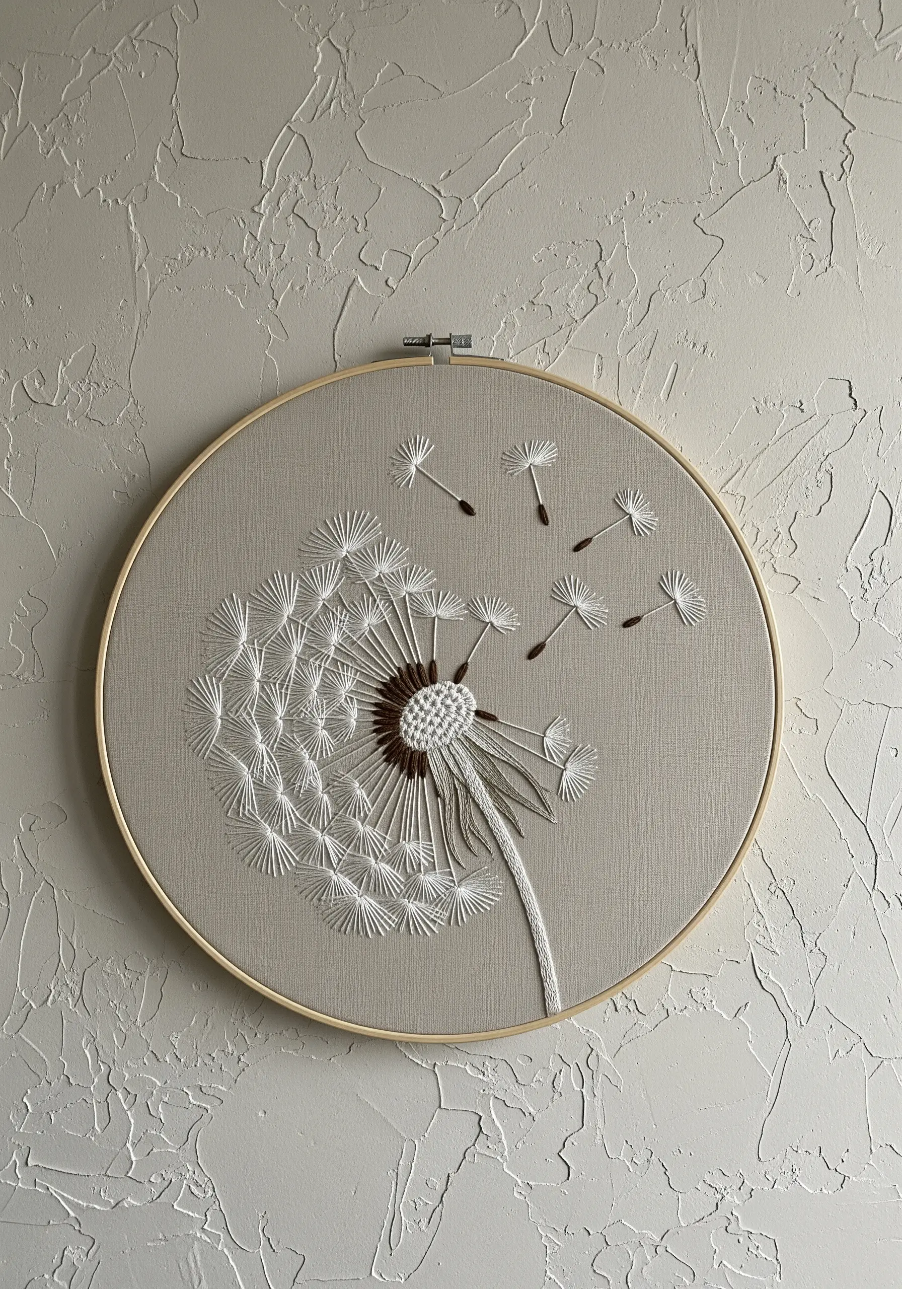 Dandelion head with seeds blowing away, embroidered in white on gray fabric.