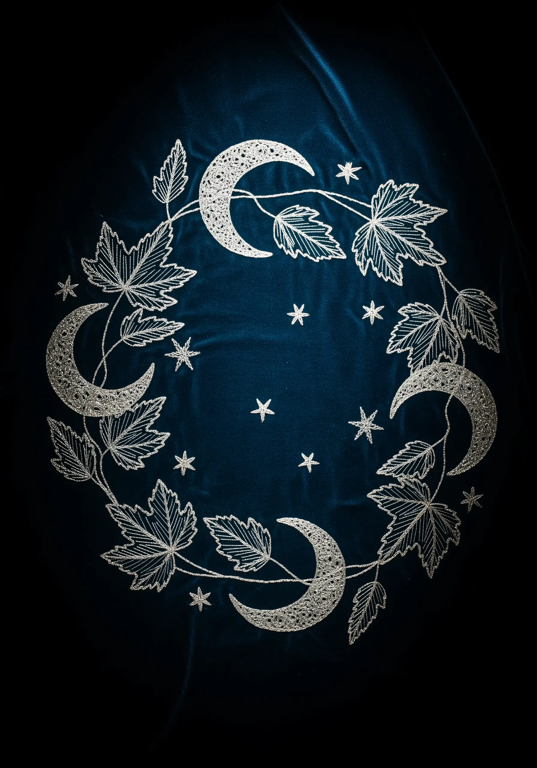 Silver thread embroidery of leaves and crescent moons forming a wreath on dark blue velvet.