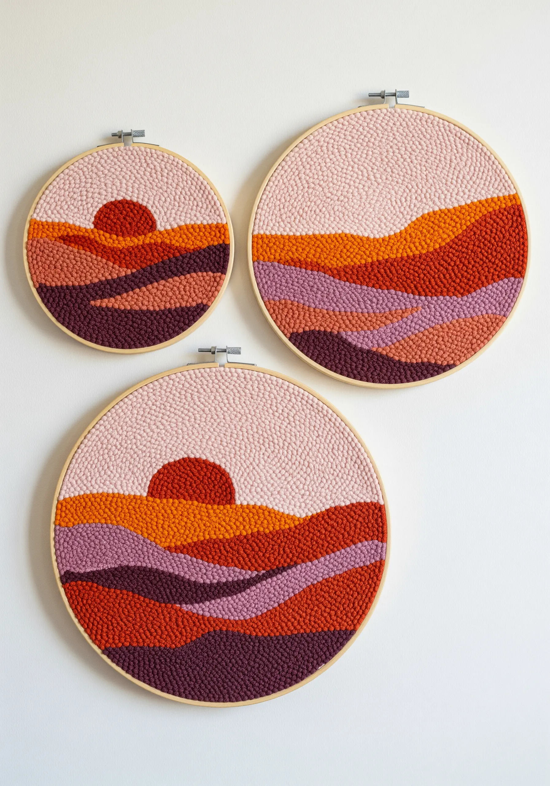 Three round punch needle hoops showing abstract sunset landscape designs.