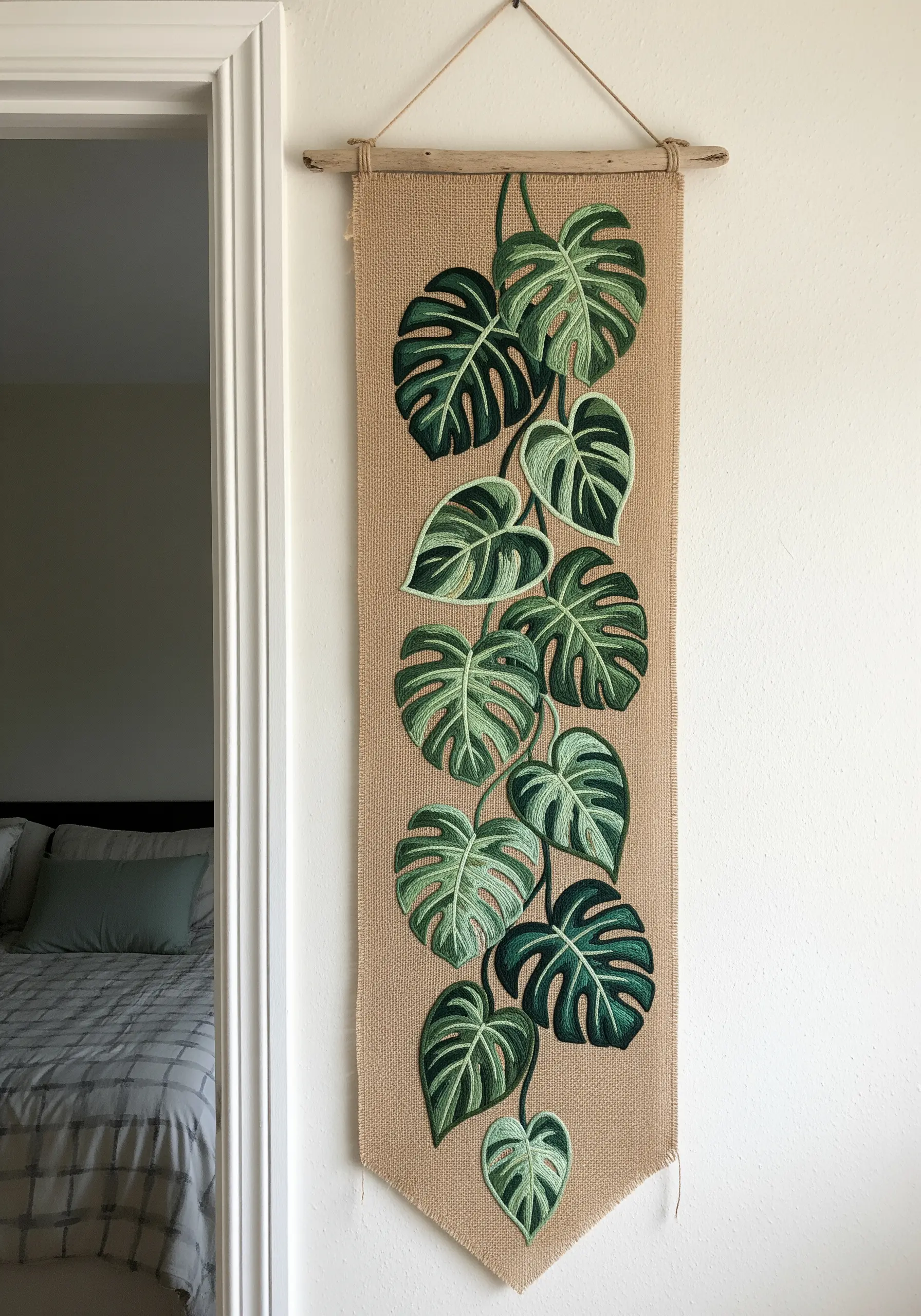 A long burlap wall hanging featuring cascading Monstera leaves in various green shades.