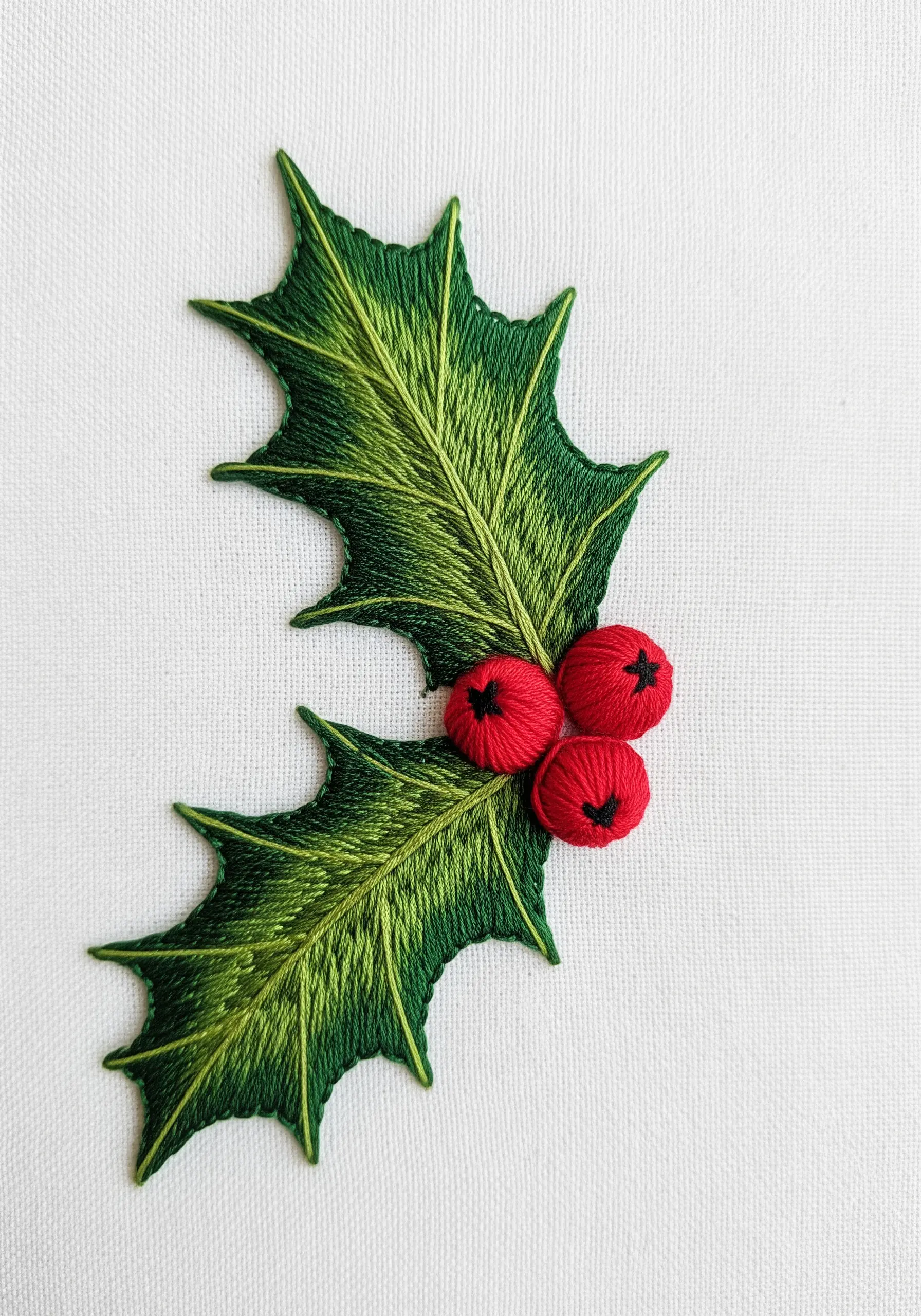 A sharp, glossy holly leaf with thread-painted gradients and dimensional red berries.