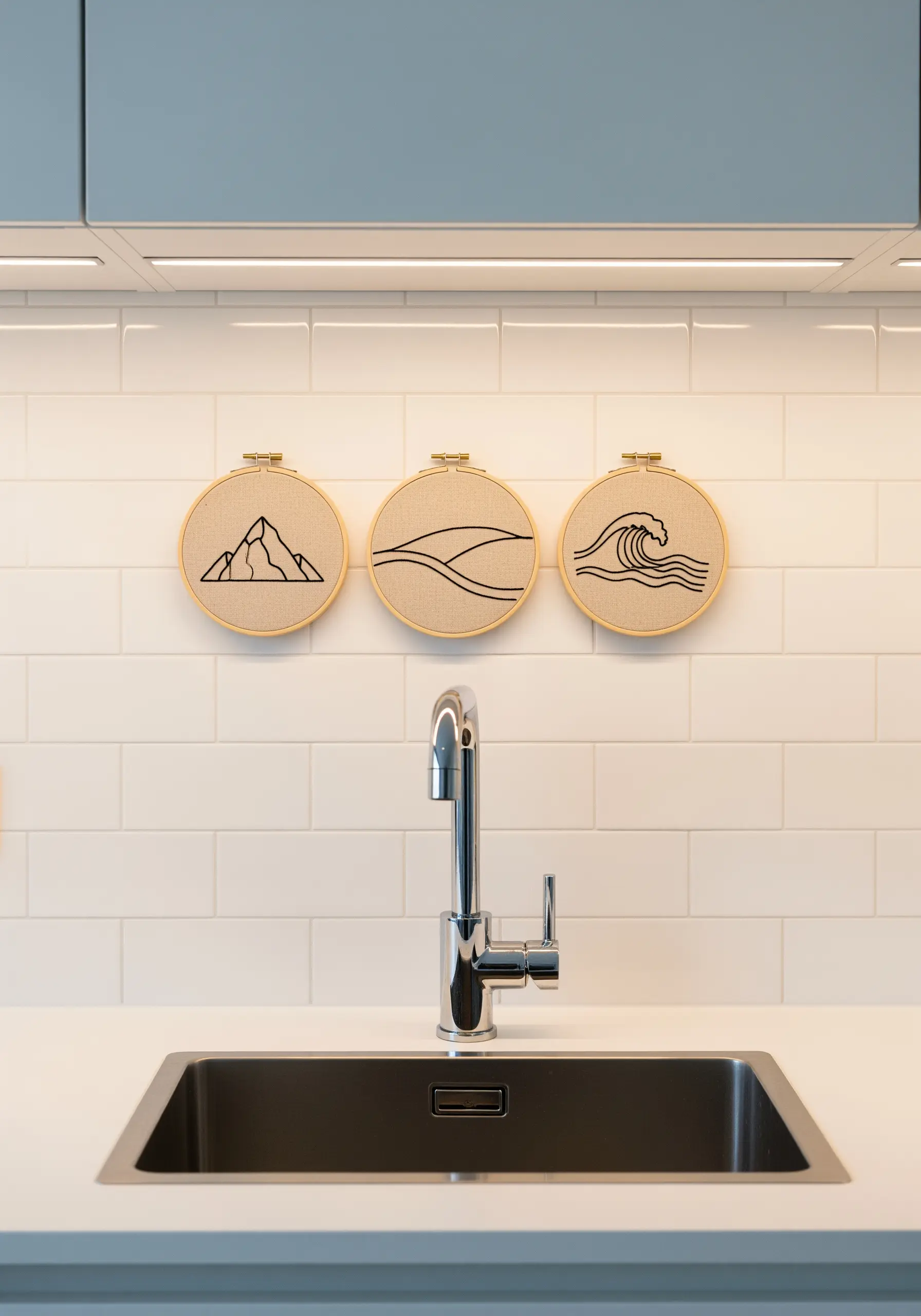 Three minimalist line-art embroidery hoops showing a mountain, dune, and wave.