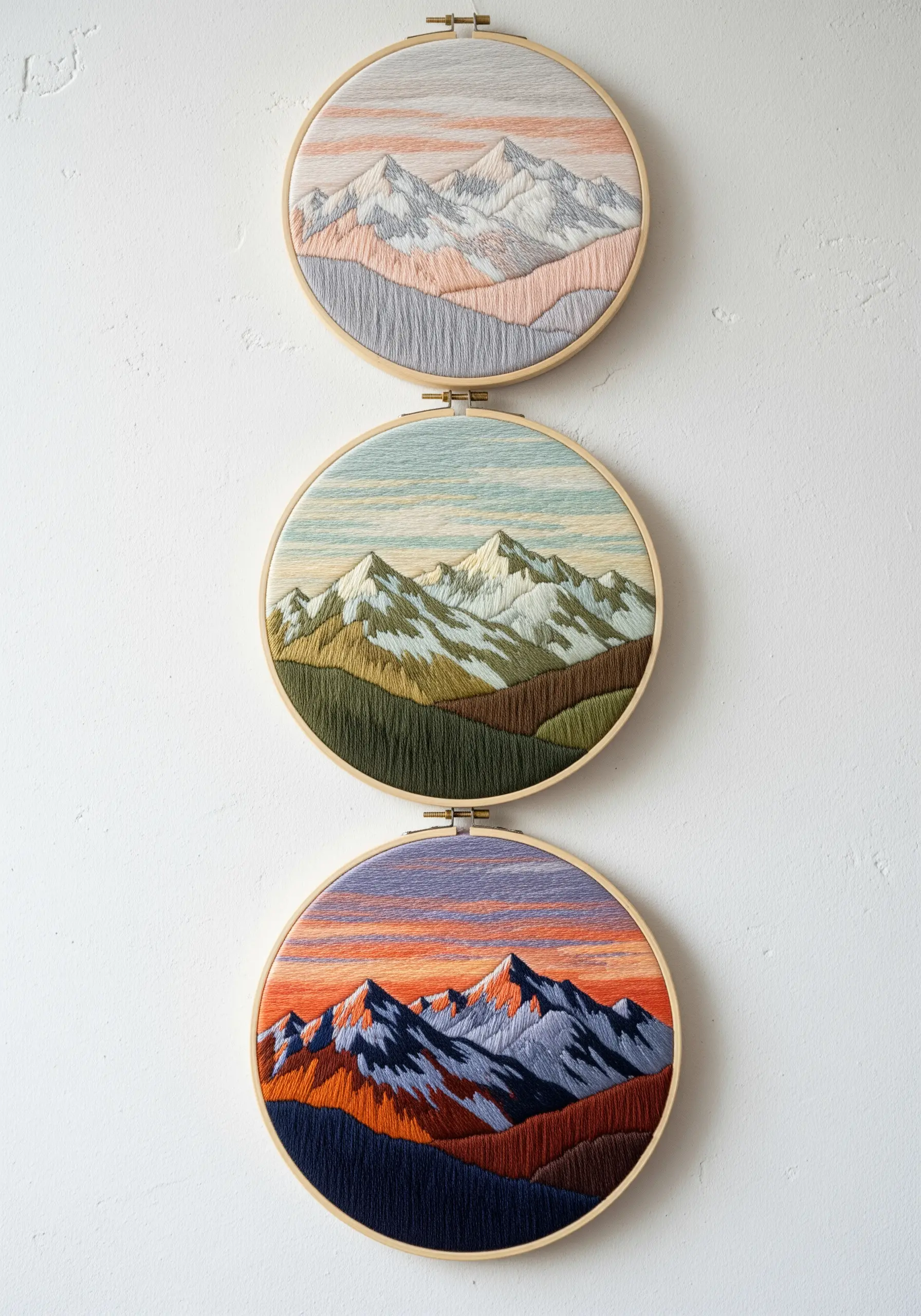 A triptych of embroidery hoops showing mountain ranges in different color palettes.