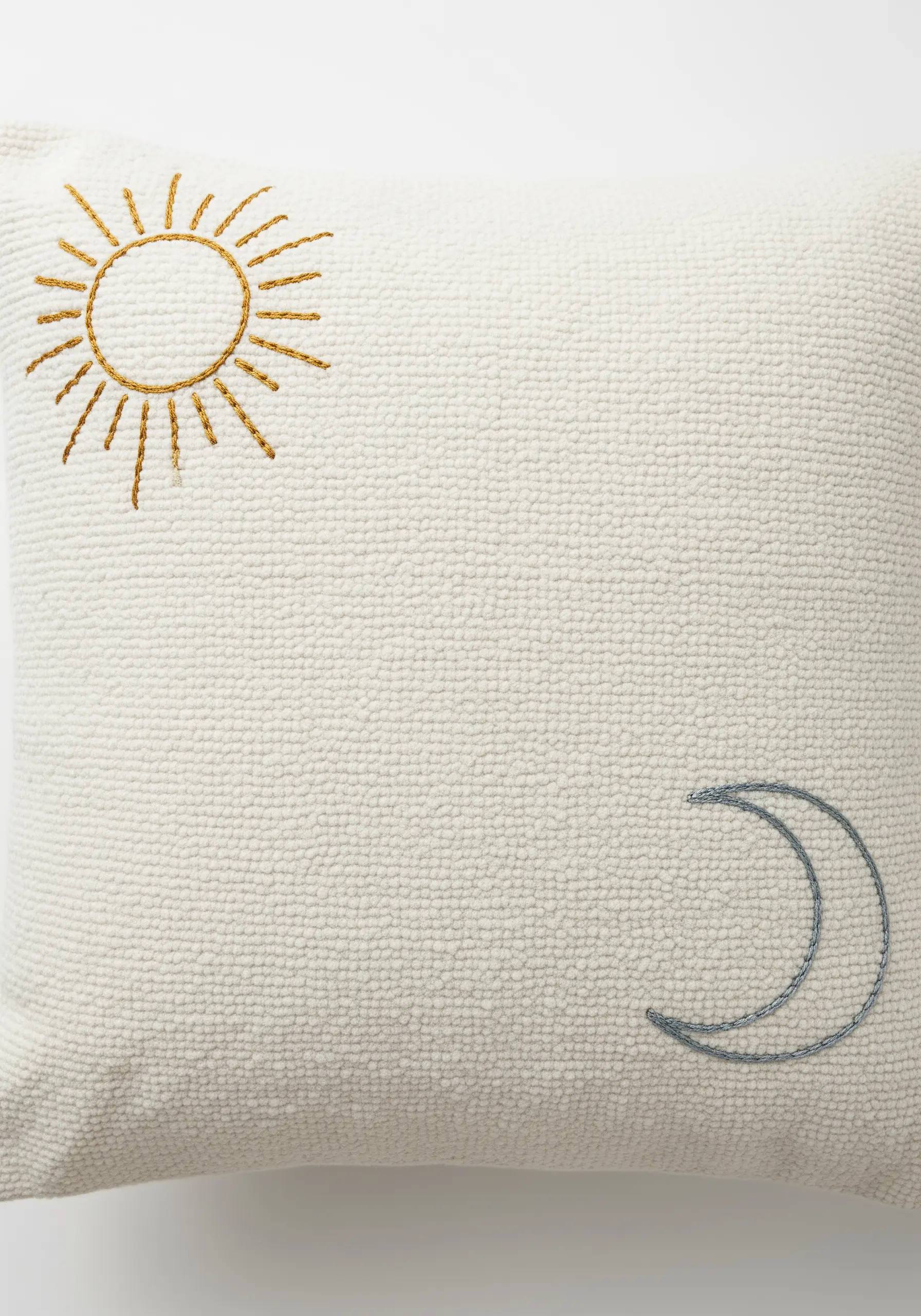 A simple sun and moon embroidered in opposite corners of a textured white cushion.