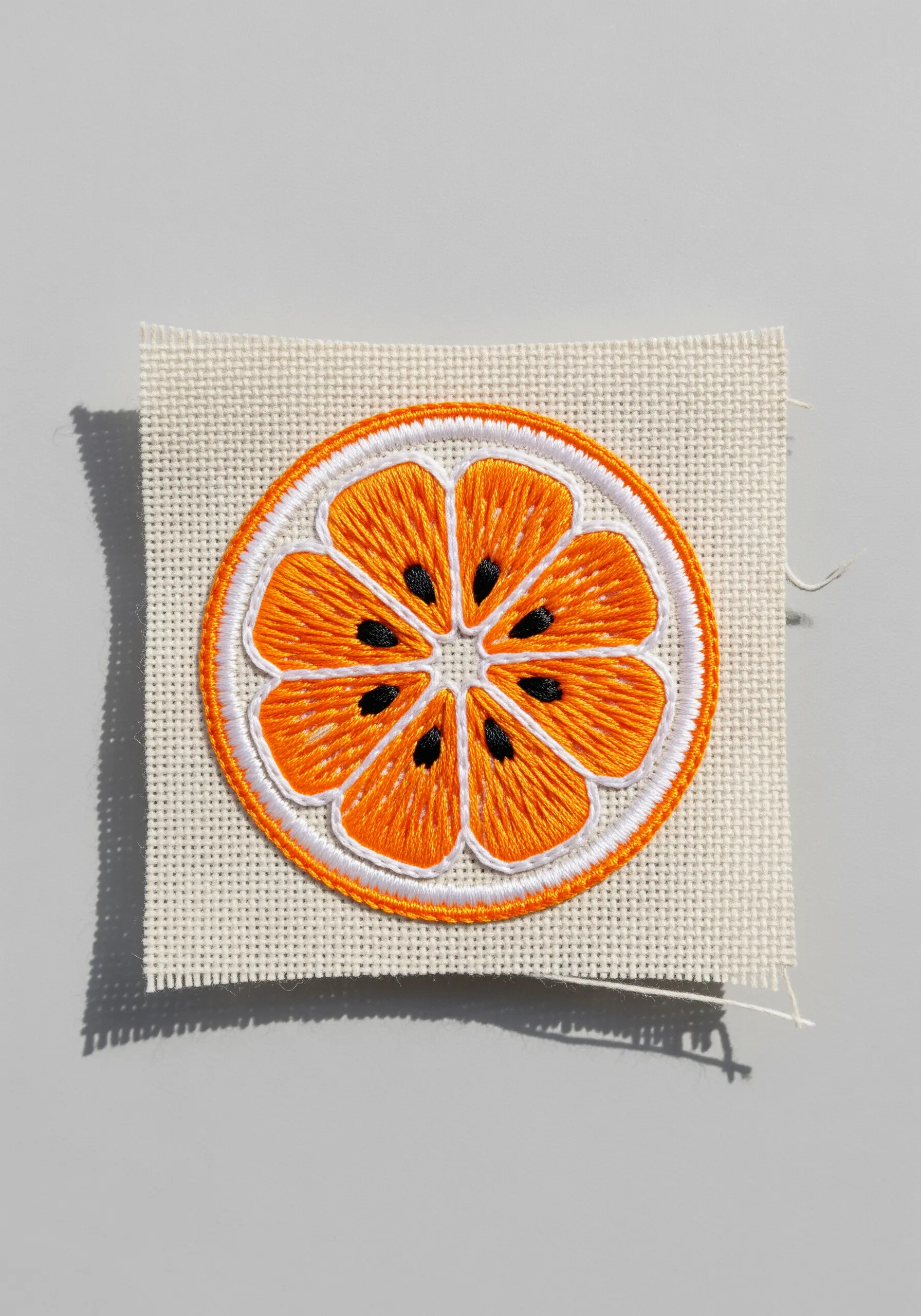 An embroidered patch of a vibrant orange slice with clearly defined satin-stitched segments.