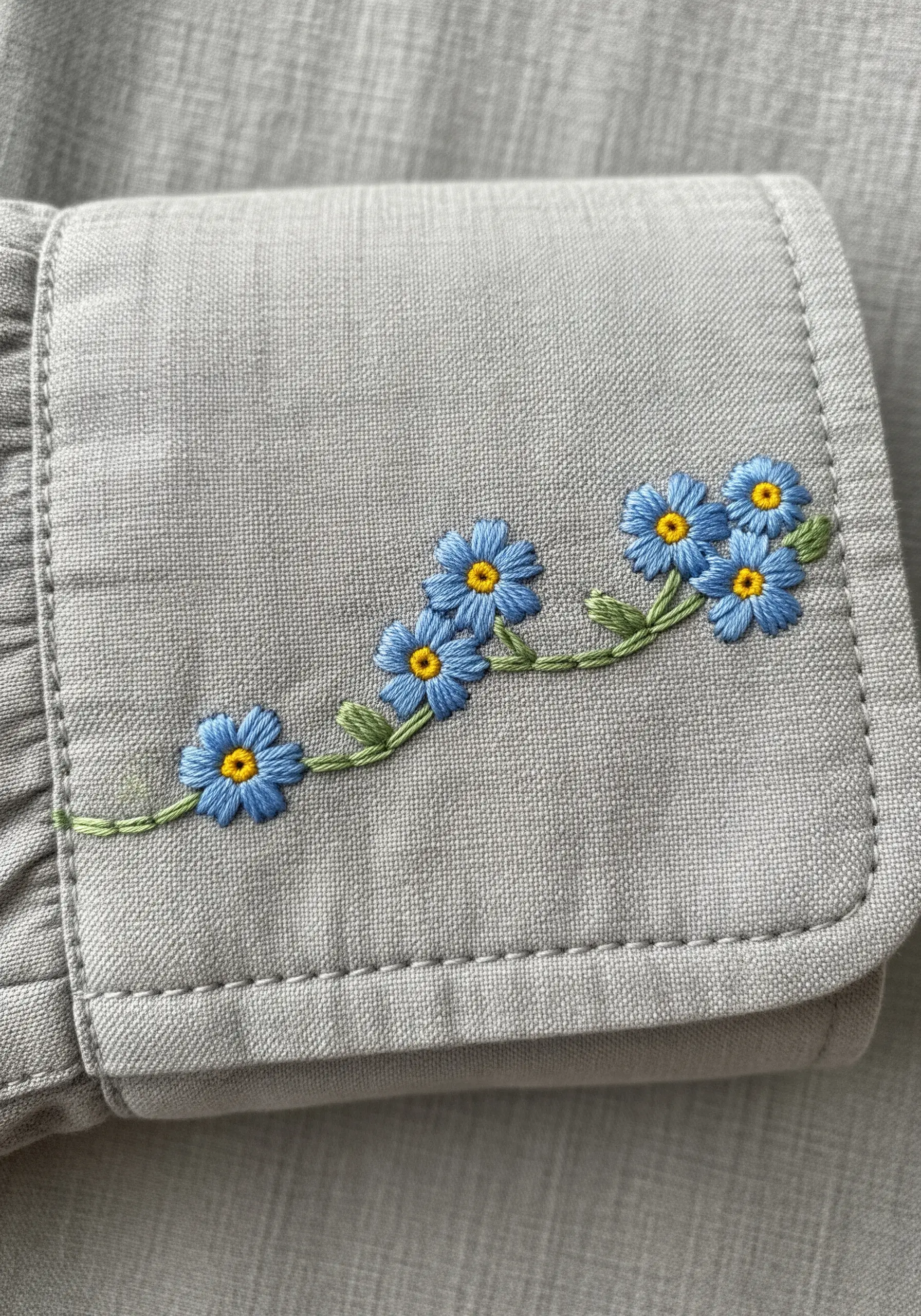 A delicate garland of blue forget-me-nots embroidered on a grey shirt cuff.