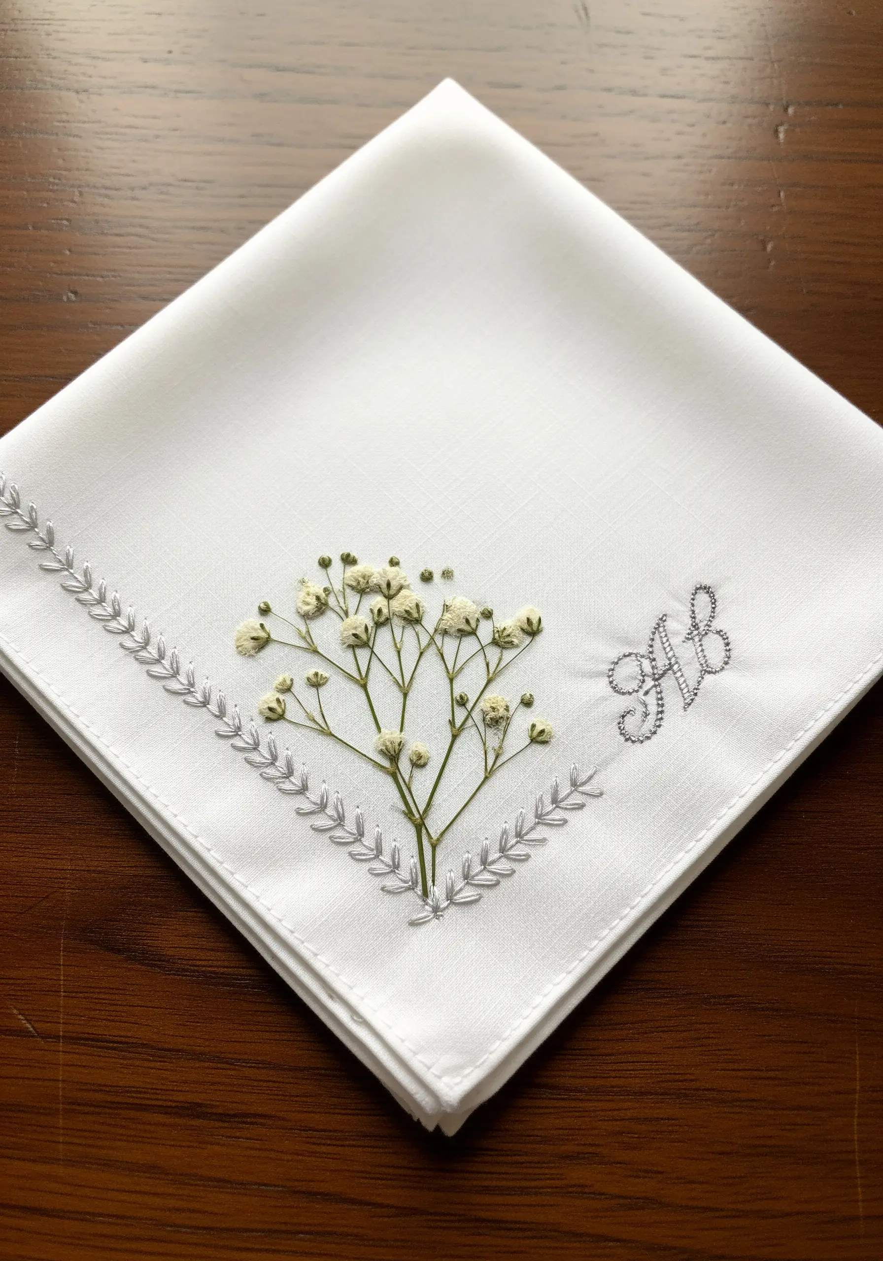 White handkerchief with a sprig of baby's breath and a silver embroidered monogram.