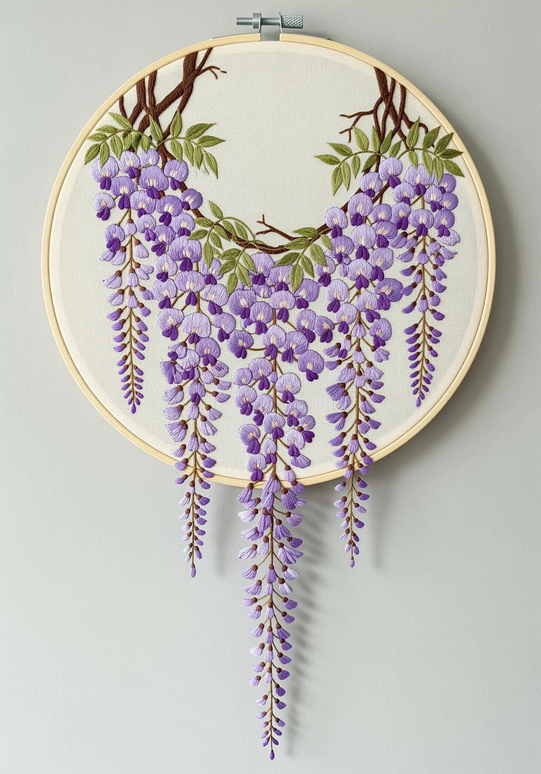 An asymmetrical embroidery of cascading purple wisteria hanging from branches in a hoop.