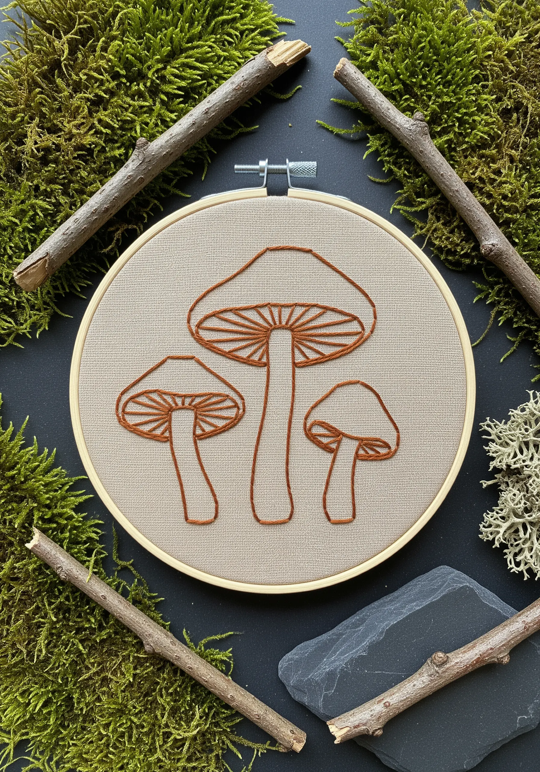 Three mushrooms outlined in brown thread on a neutral beige fabric.