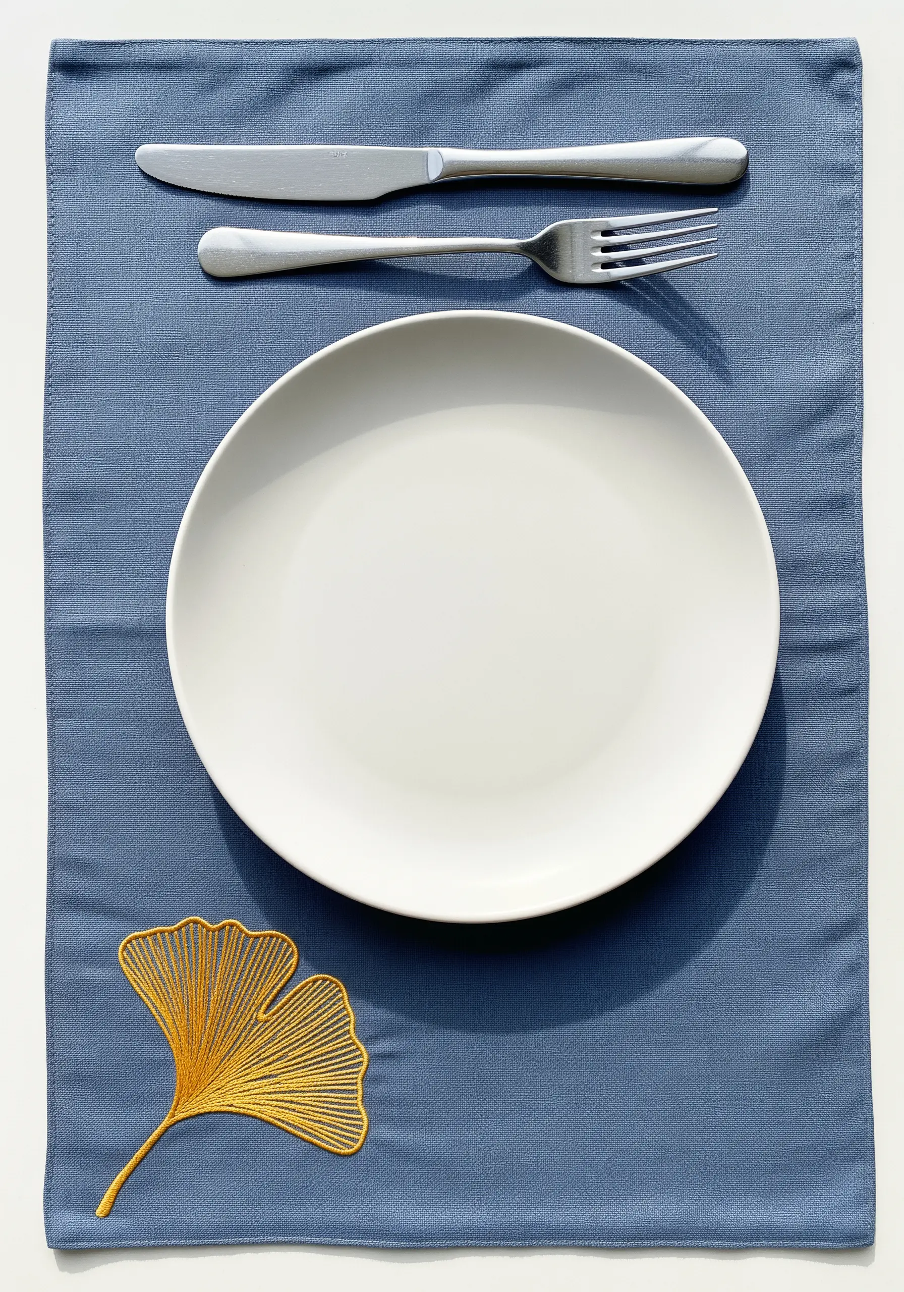 A golden-yellow ginkgo leaf embroidered with directional satin stitch on a blue placemat.