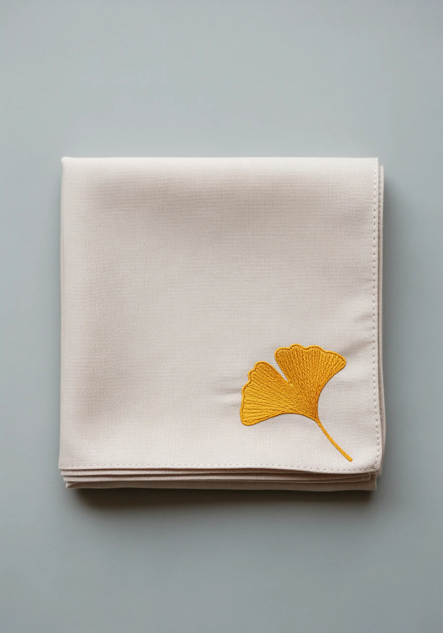 A single golden yellow ginkgo leaf embroidered on a folded natural napkin.