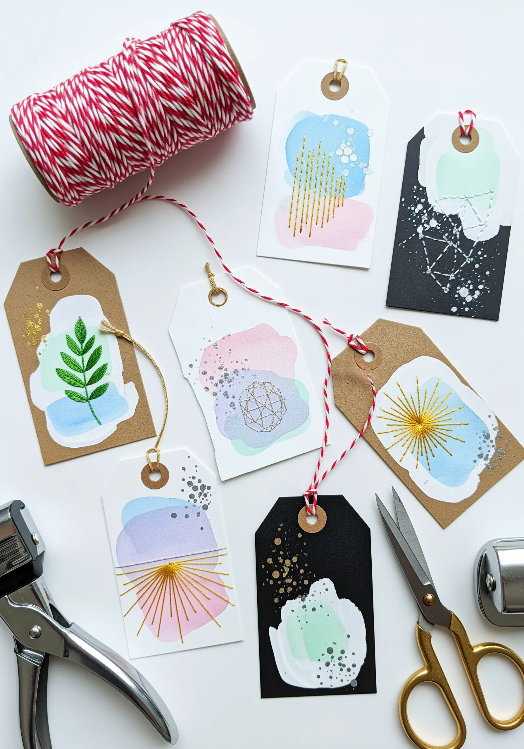 Paper gift tags decorated with watercolor washes and gold thread embroidery details.