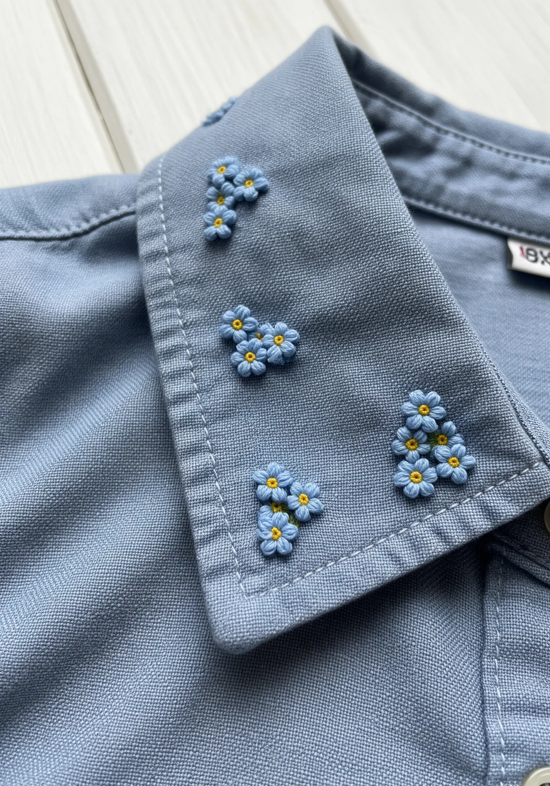 Clusters of tiny blue embroidered forget-me-nots with yellow centers on a blue shirt collar.