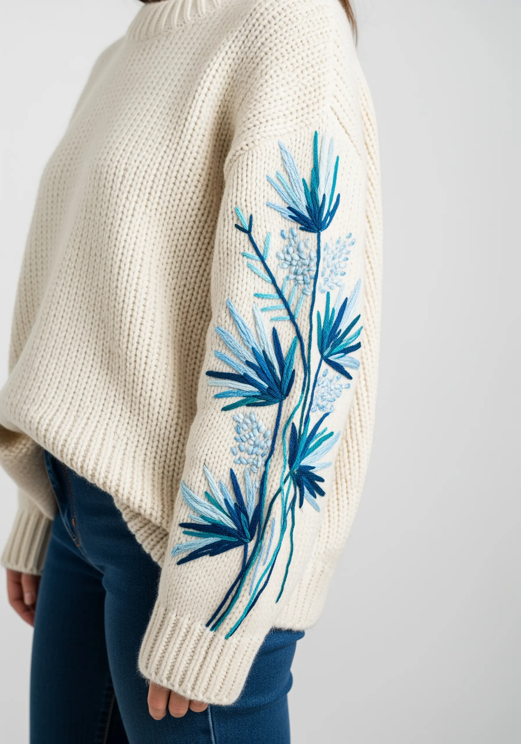 Abstract blue floral embroidery stitched down the sleeve of a chunky cream sweater