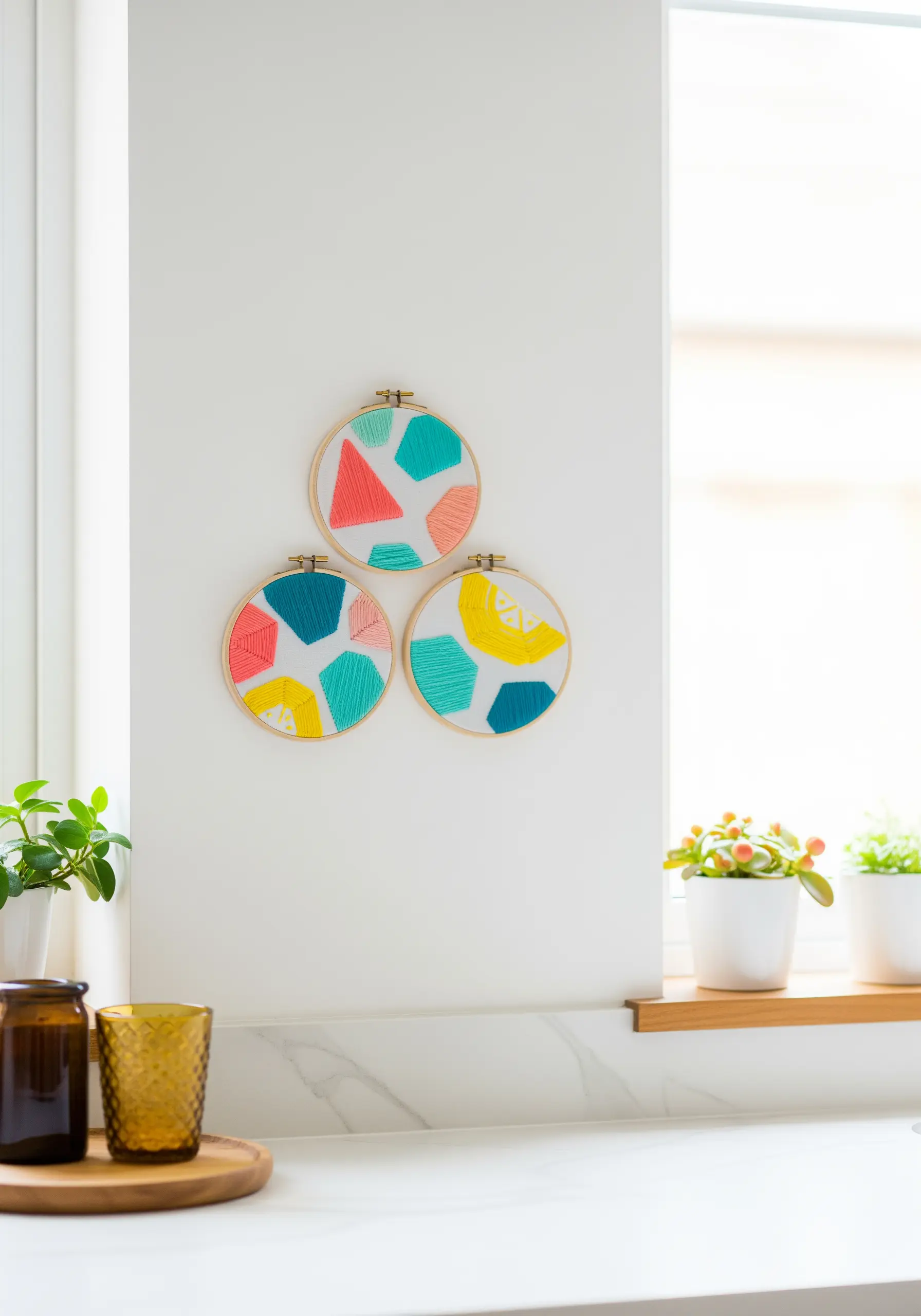 Three small embroidery hoops with bright, abstract color-blocked shapes in teal, pink, and yellow.