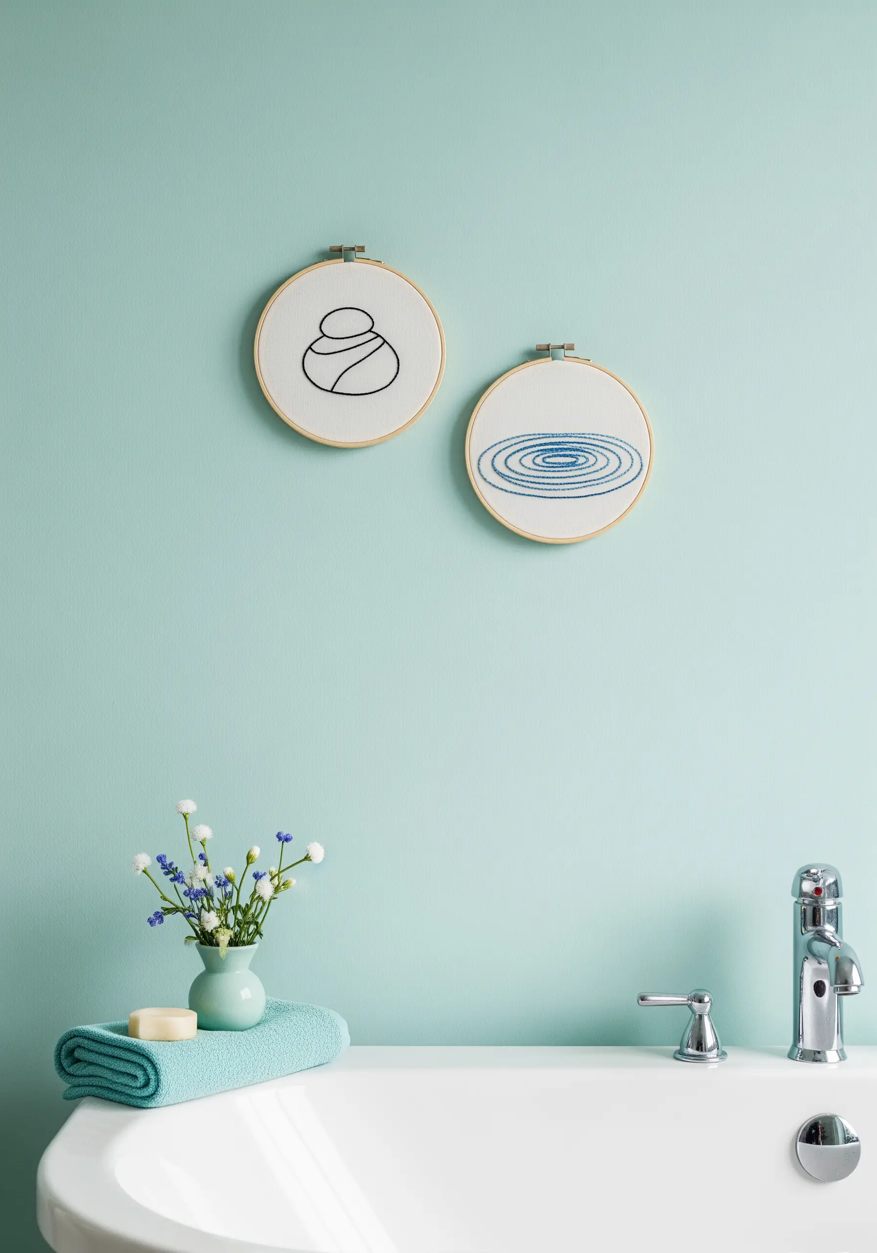 Two small embroidery hoops above a bathtub, one with stacked zen stones, one with water ripples.