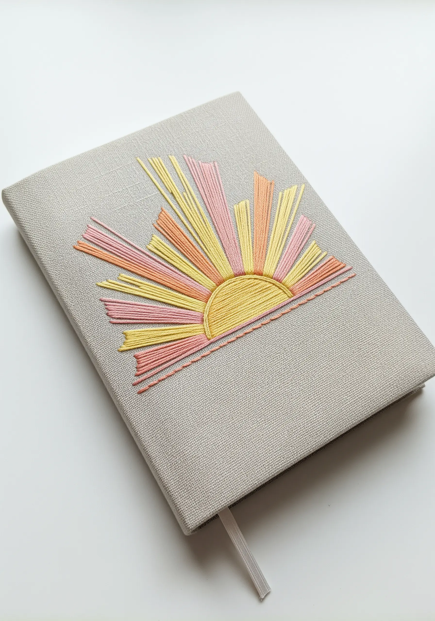 A grey linen journal with a pastel sunburst embroidered on the cover.