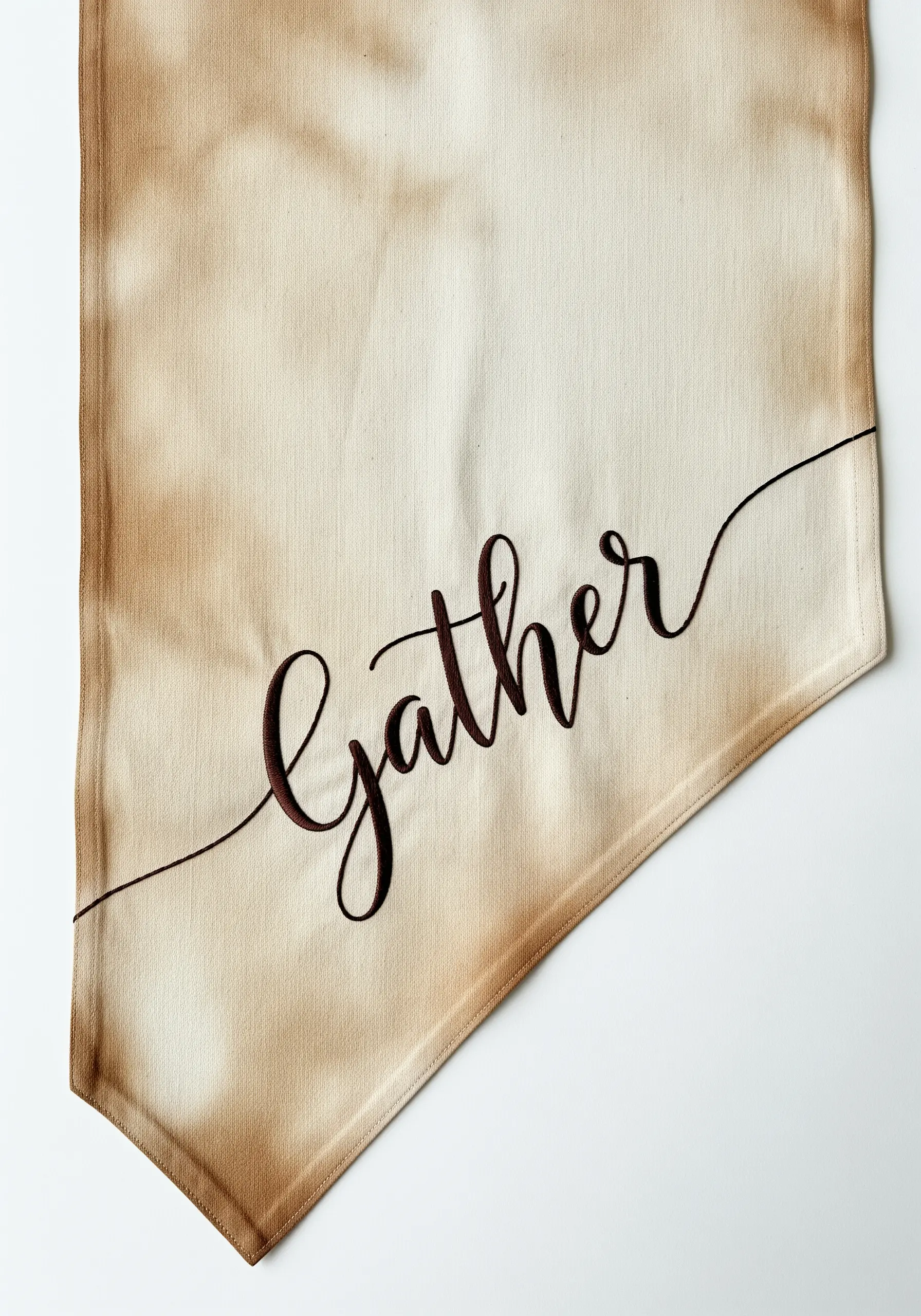 The word 'Gather' embroidered in elegant script on a tea-stained table runner.
