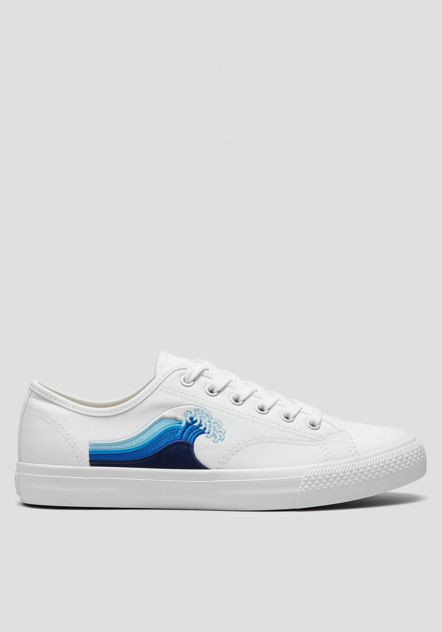 A stylized blue wave embroidered on the side of a white canvas sneaker.
