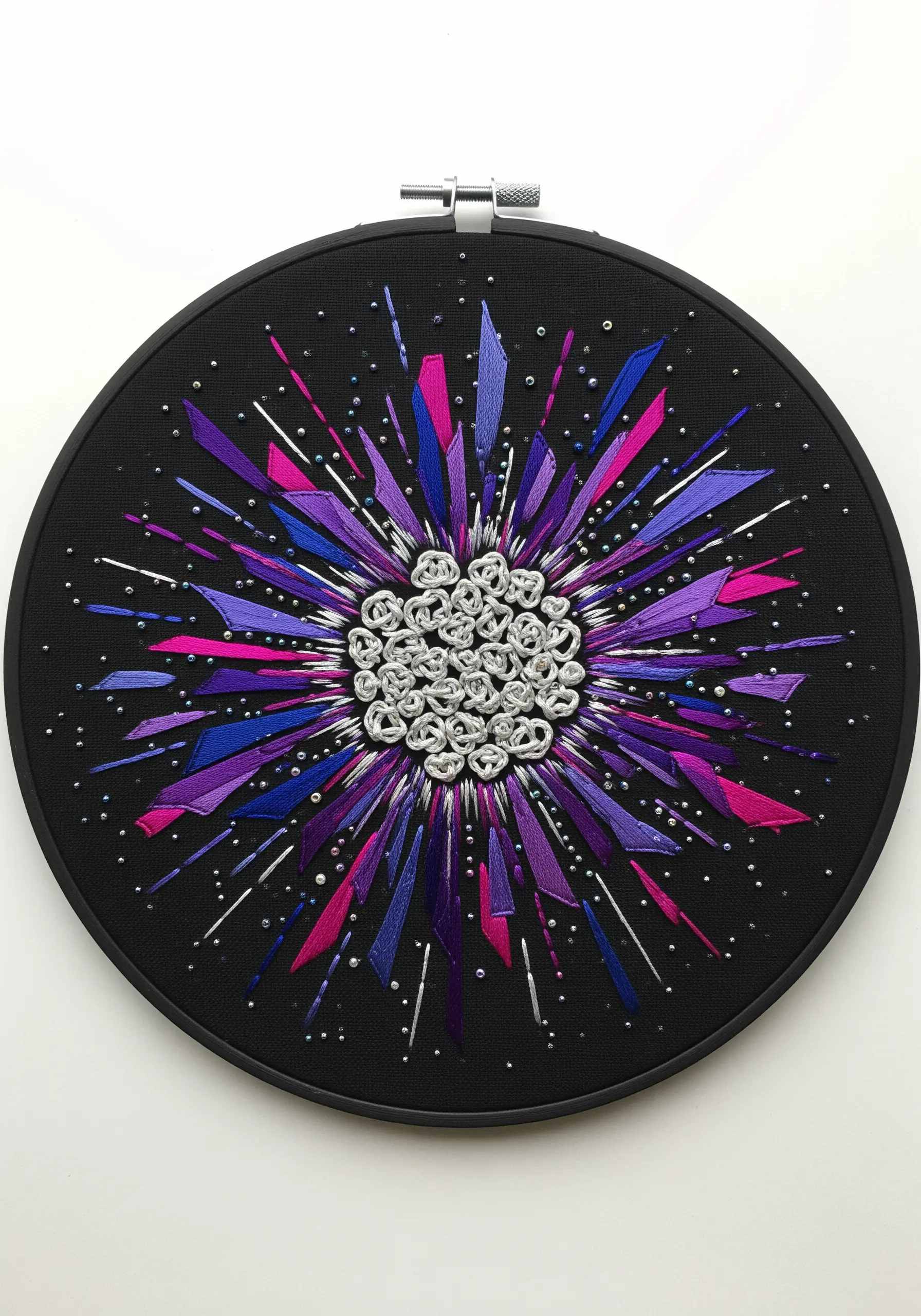 A starburst embroidery with purple and pink satin-stitched rays and a silver knot center.
