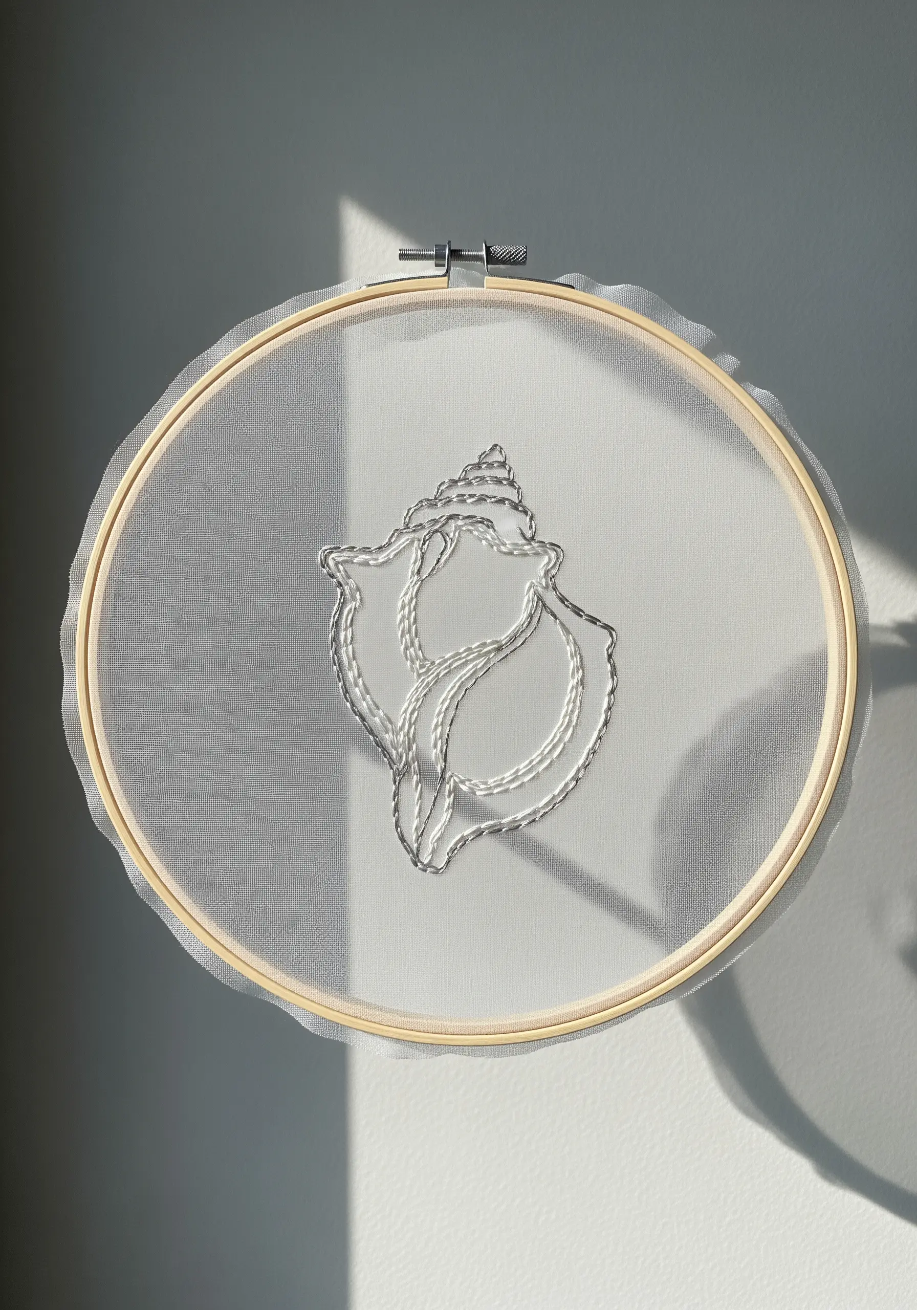 Outline of a seashell stitched in white thread on sheer, transparent fabric.