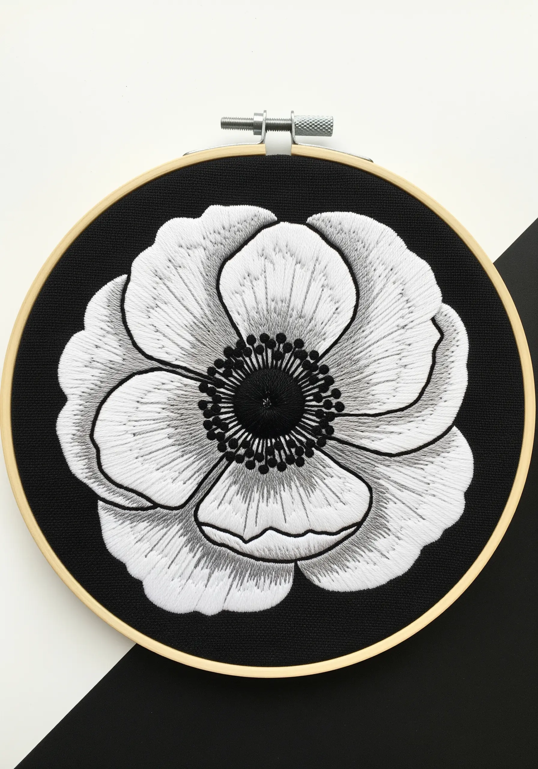 A black-and-white embroidered anemone flower, showing detailed shading on a black background.