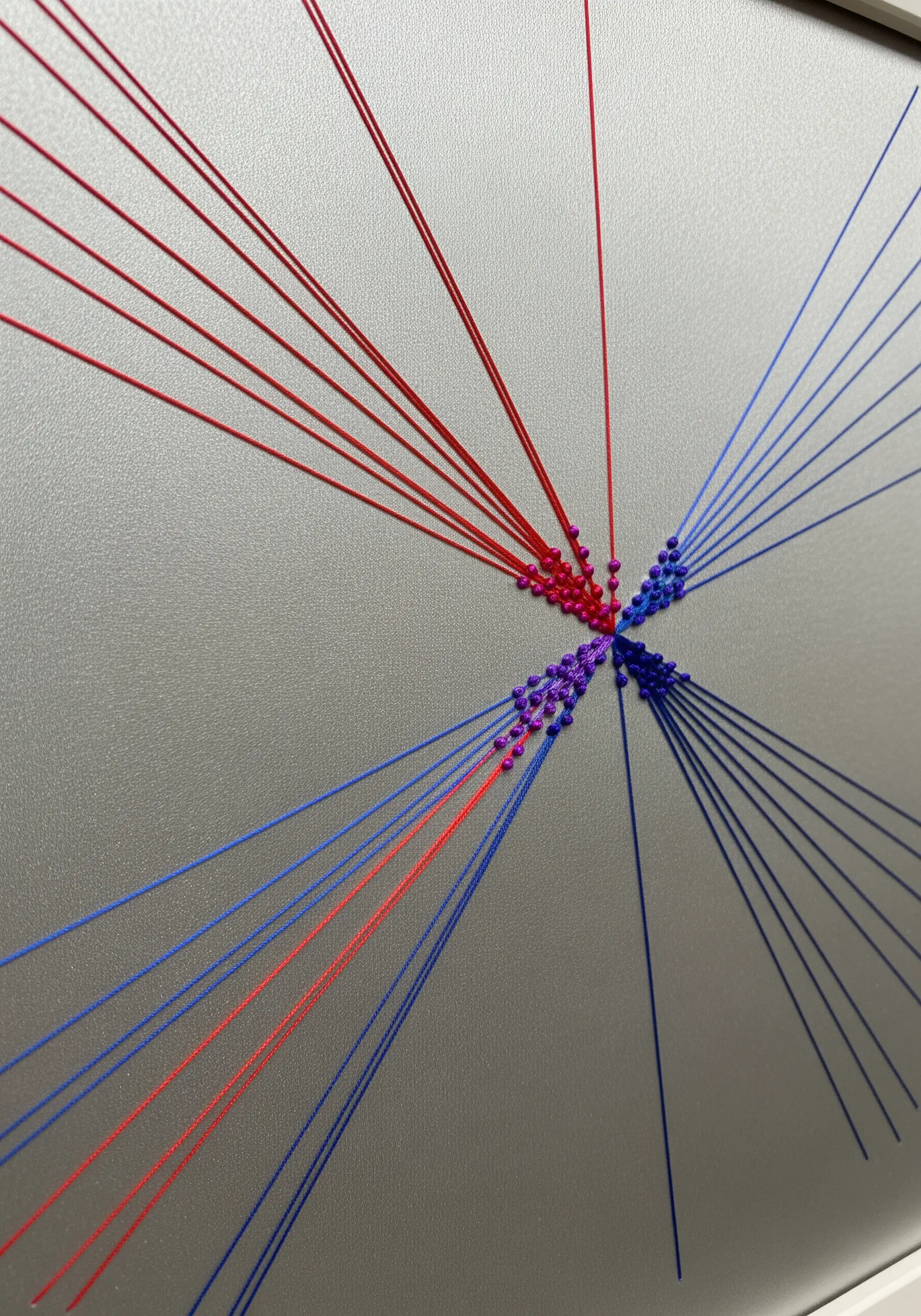 A 3D string art piece with red, blue, and purple threads stretched between pins.