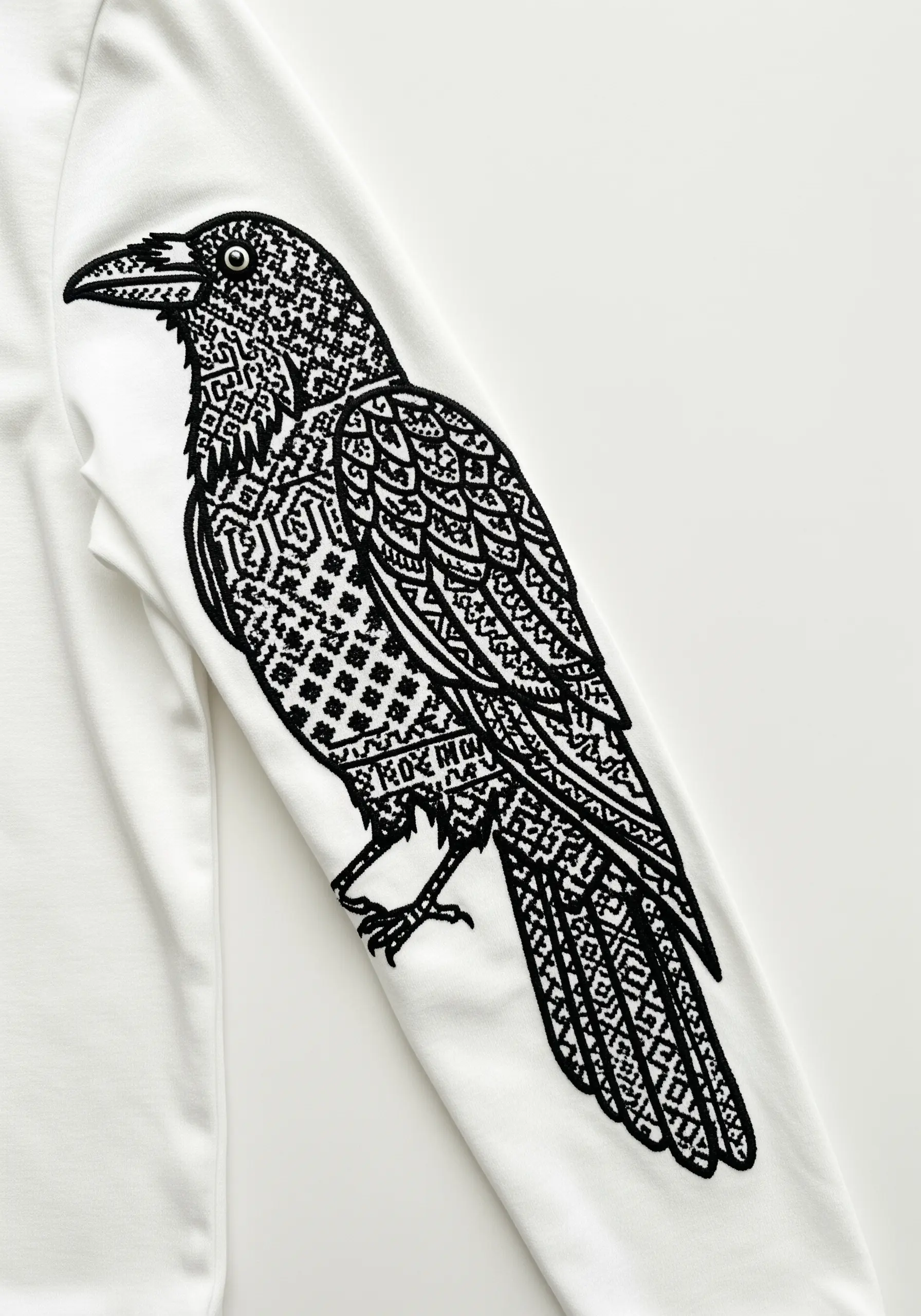 A large raven embroidered on a white sleeve, its body filled with complex geometric blackwork patterns.