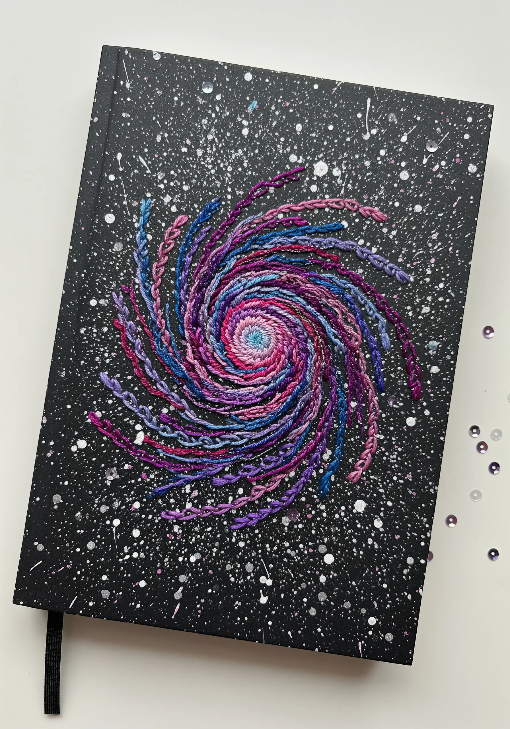 A swirling galaxy embroidered with braided stitches in purple, blue, and pink variegated thread.