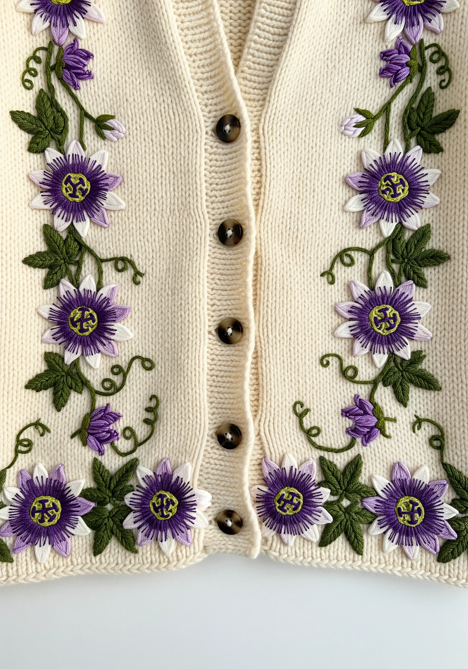 Symmetrical passion flower vine embroidery framing the button placket of a cream knit cardigan
