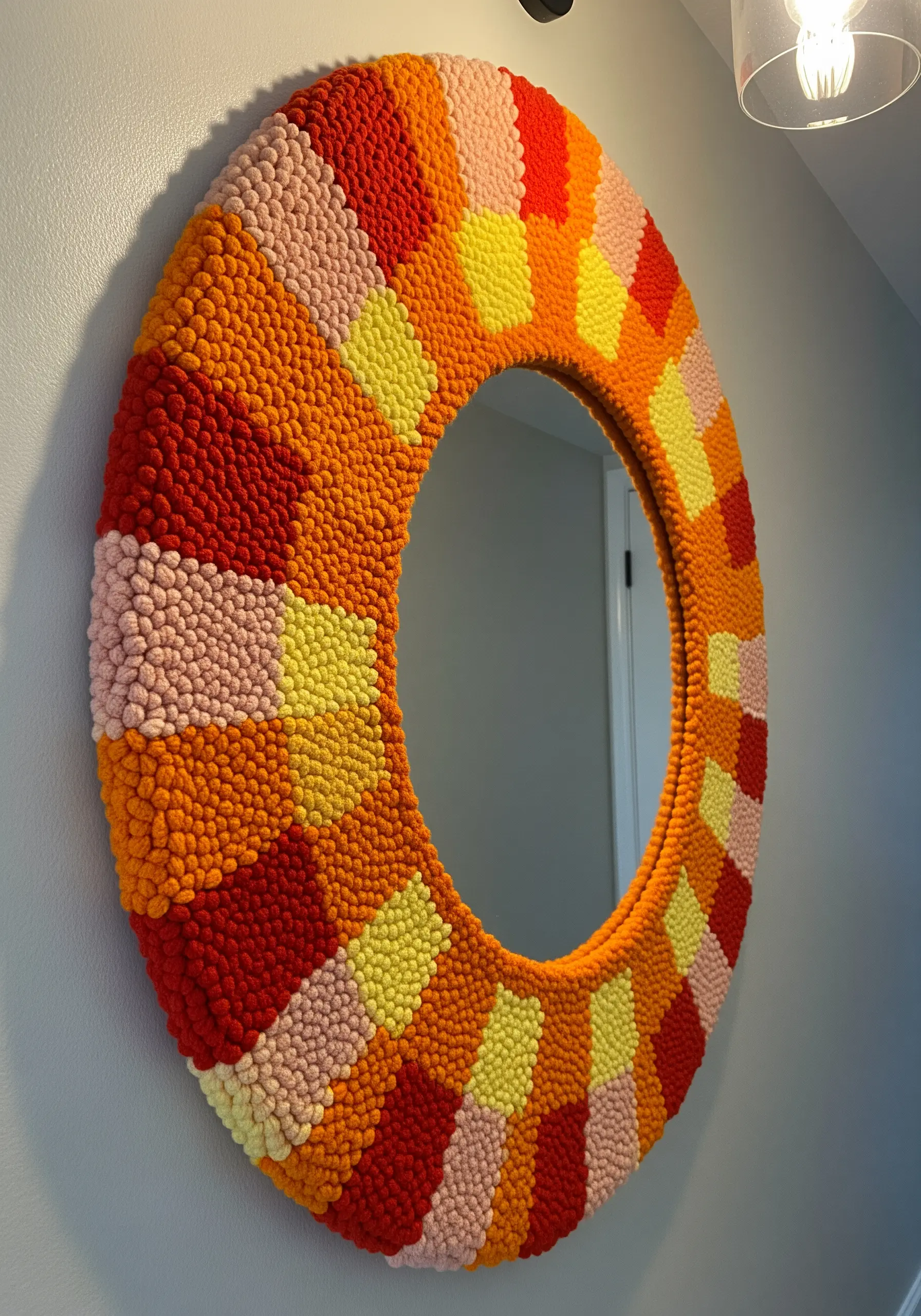 A round mirror framed with a colorful, blocky punch needle design in orange, red, and yellow.