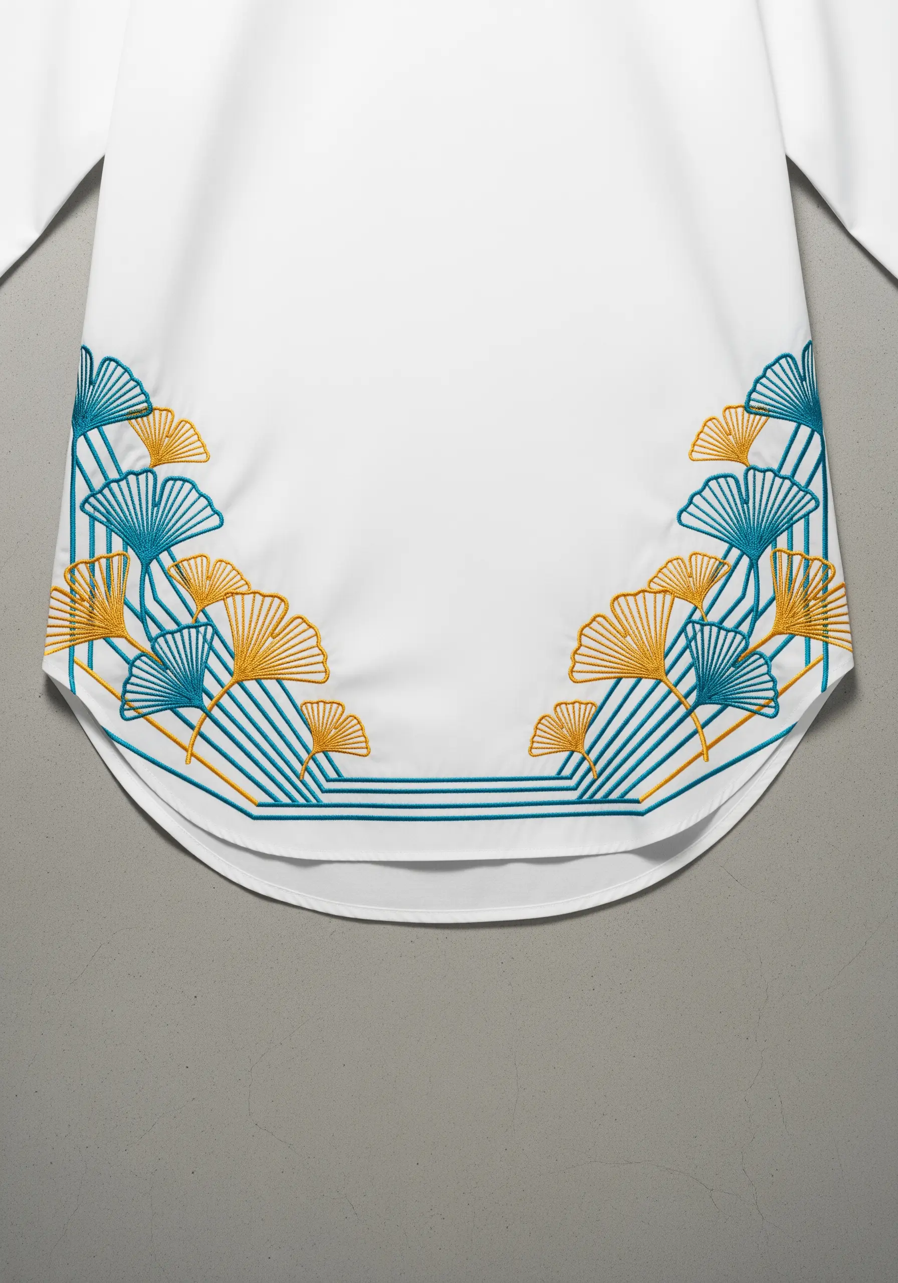 Graphic ginkgo leaf embroidery in teal and gold on a white shirt hem