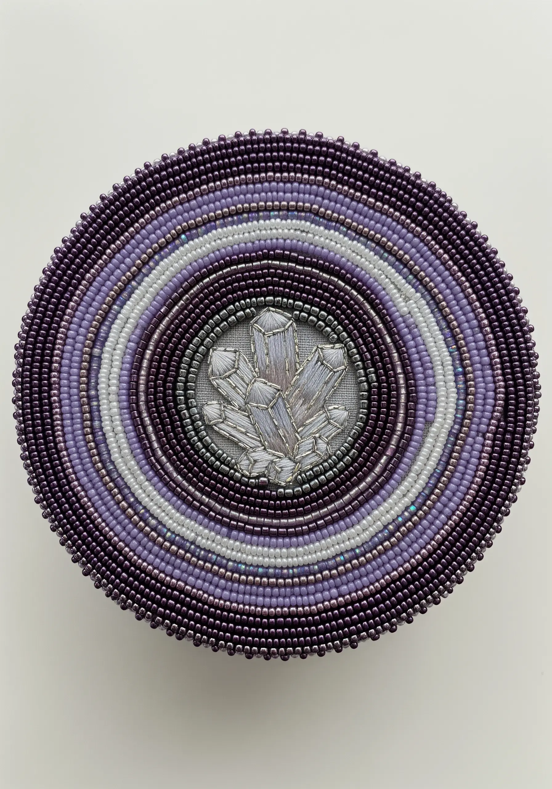 An embroidered crystal motif at the center of a circular lid framed by rings of purple seed beads
