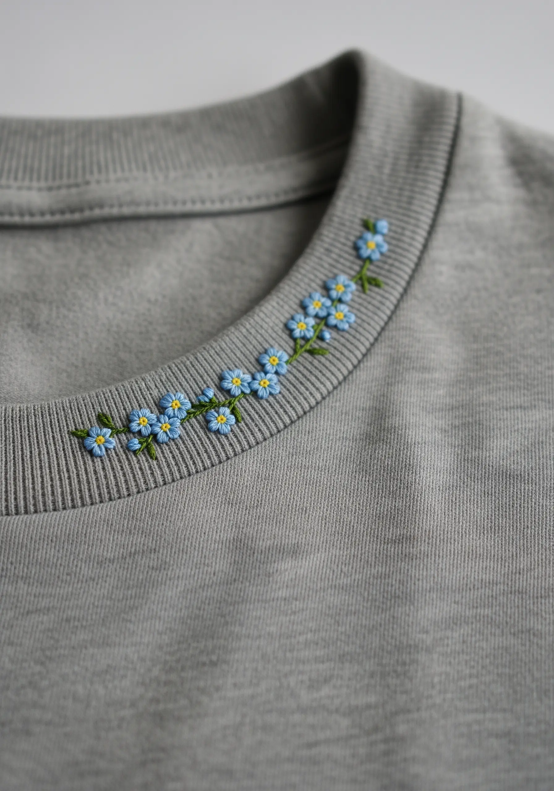 Blue forget-me-not flowers embroidered along the collar of a grey sweatshirt.