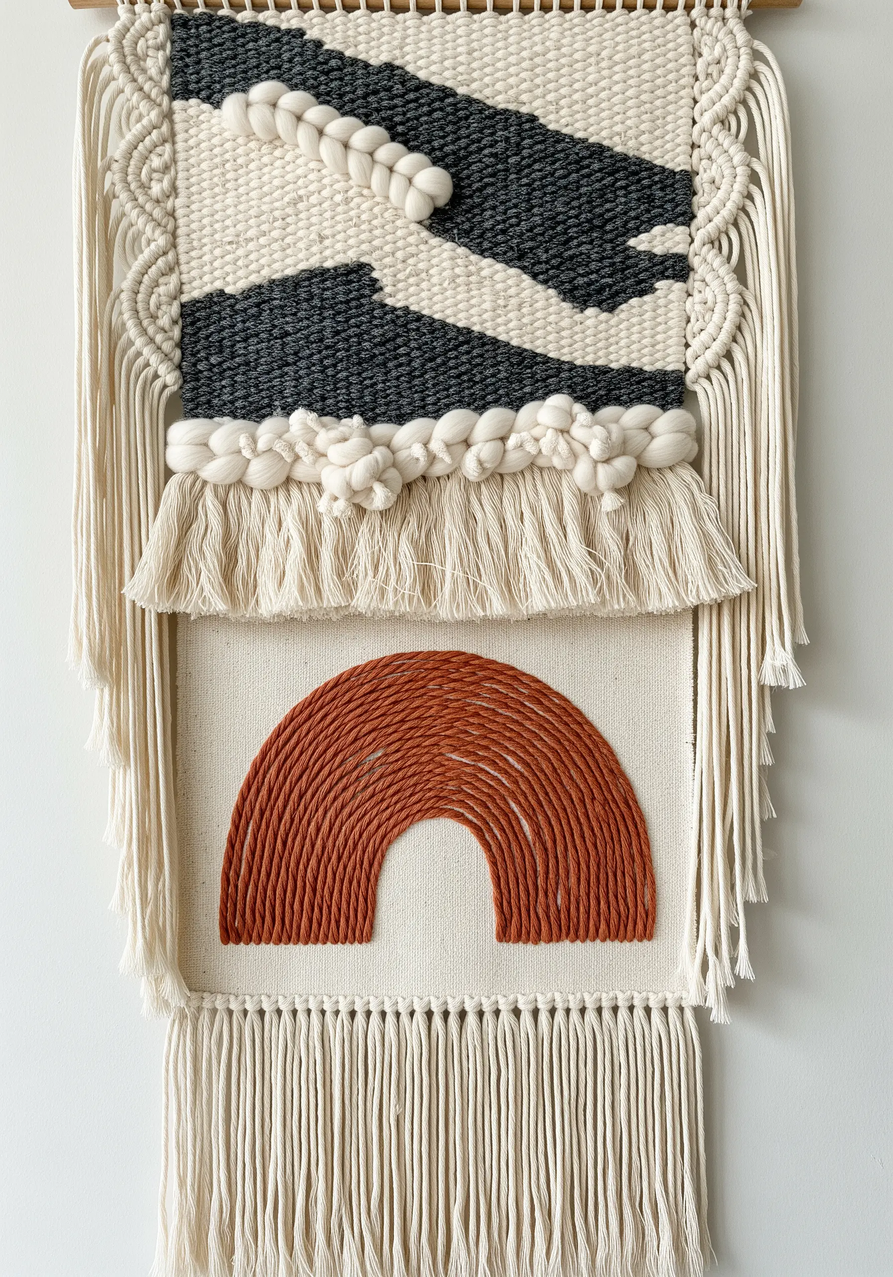 A mixed-media wall hanging with weaving, macrame, and an embroidered rainbow section.