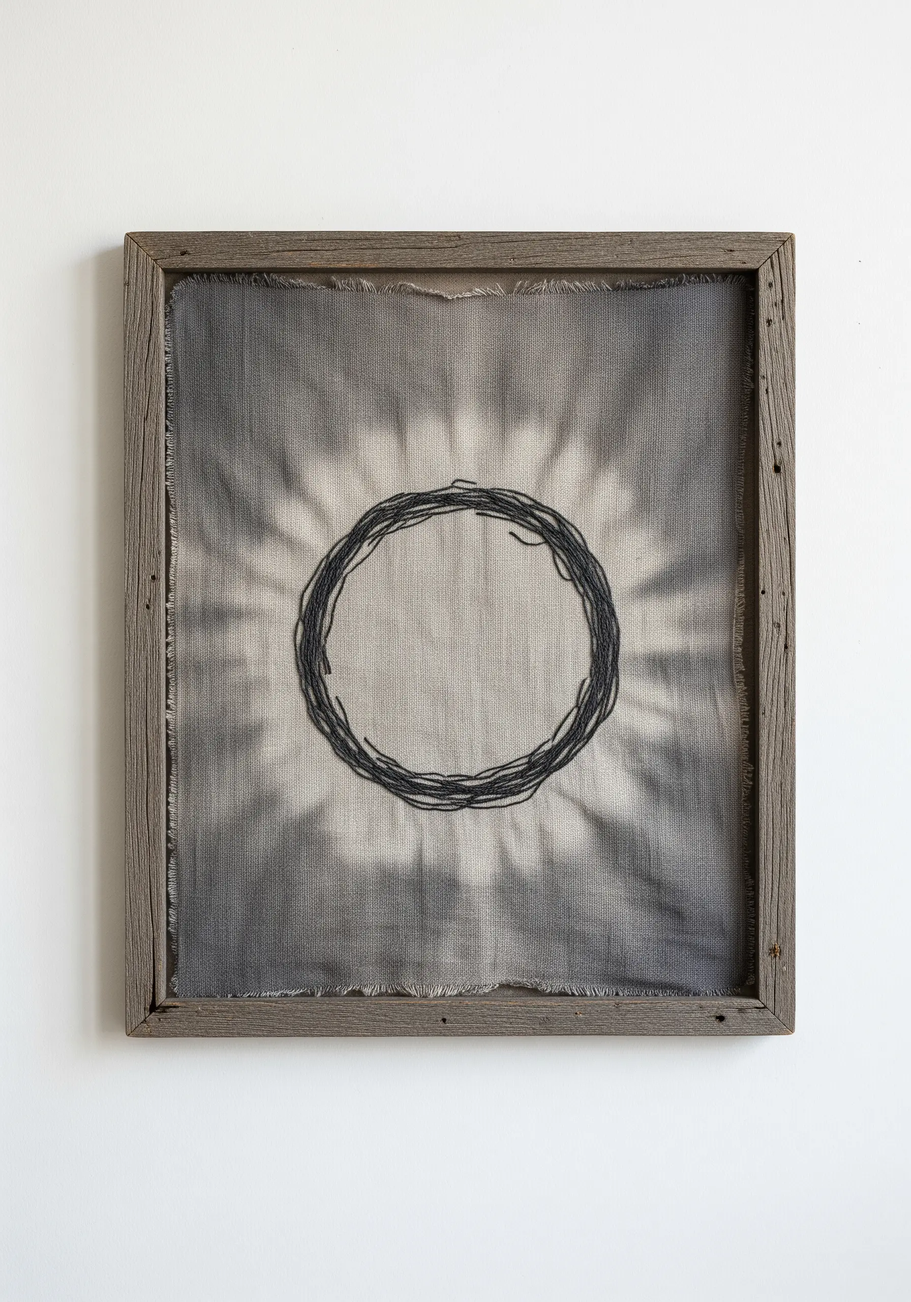 A simple embroidered circle on tie-dyed fabric presented in a rustic wooden frame.